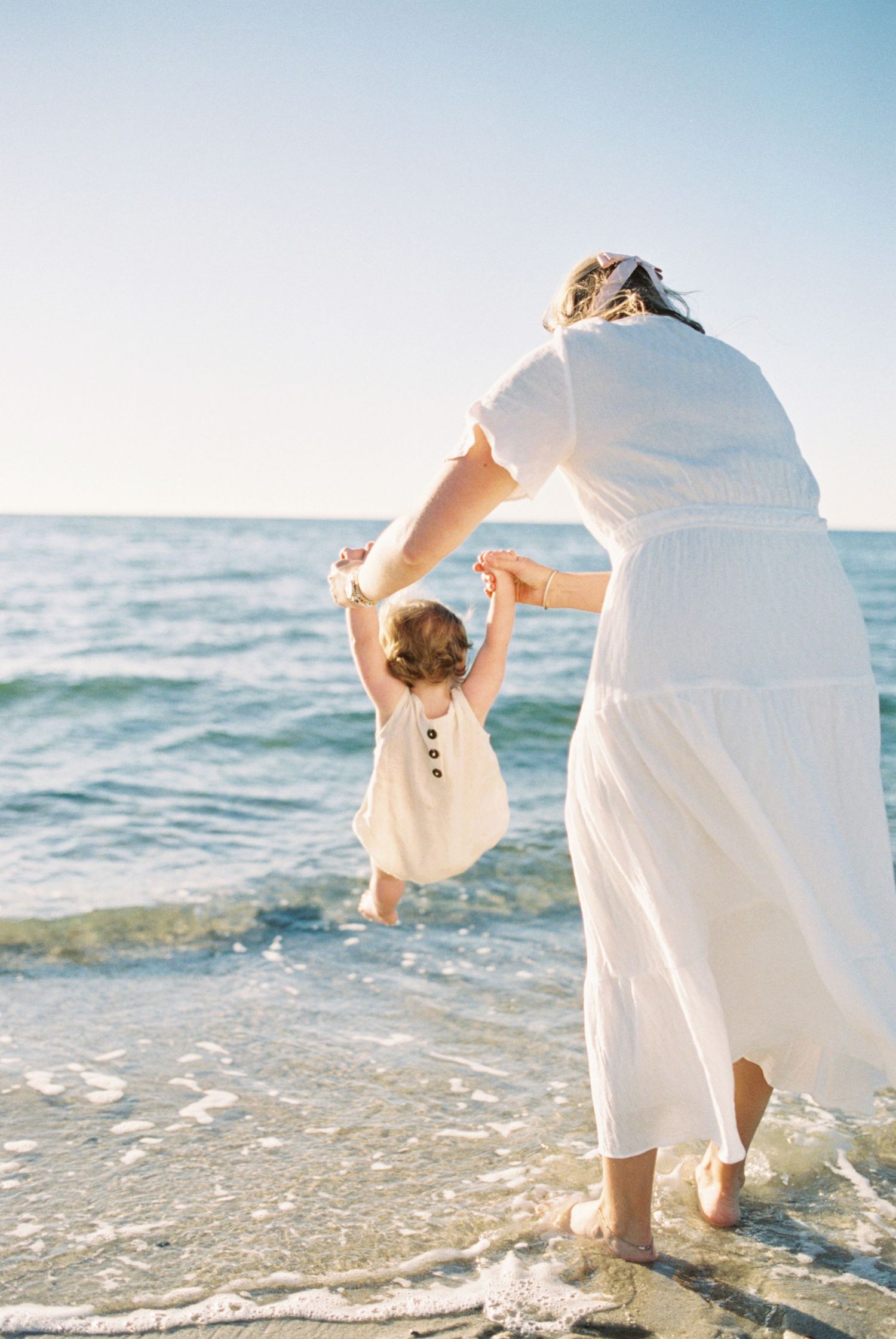 People in white clothing playing and splashing at the beach during golden hour.