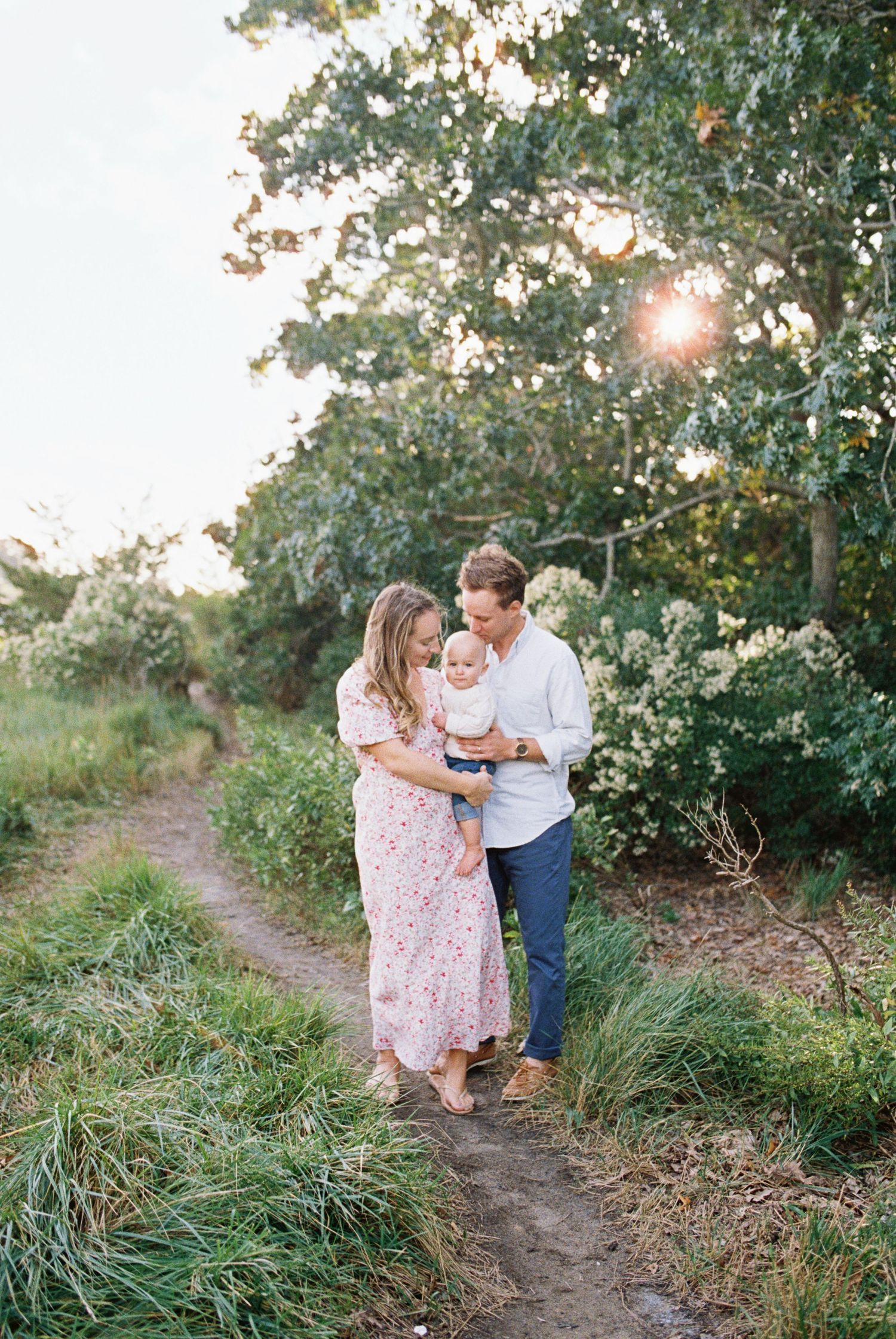 Couple walking along a nature path surrounded by lush greenery and sunlight.