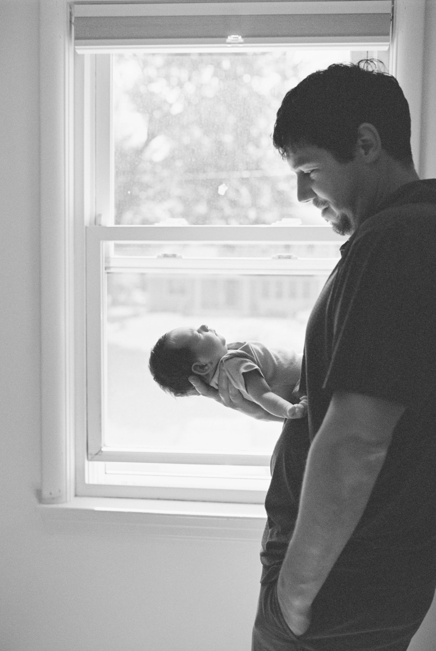 Indoor photoshoot of parent holding newborn baby near window.