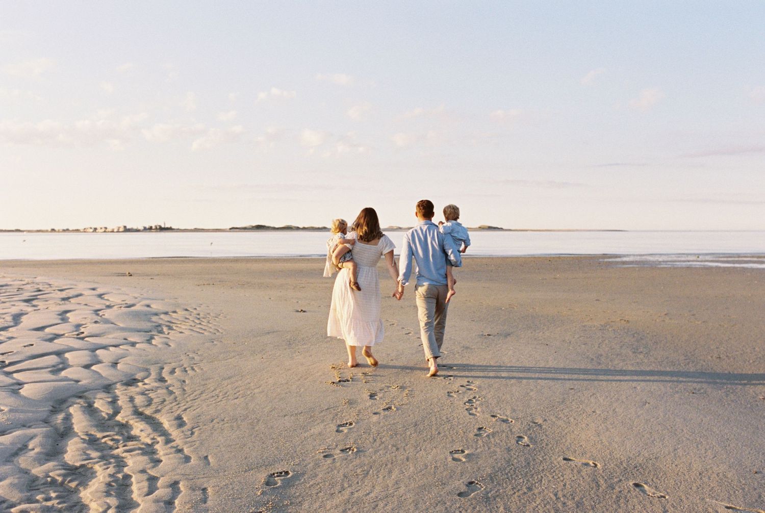 A panoramic view of people walking along a vast empty beach at sunset with long shadows cast on the sand.