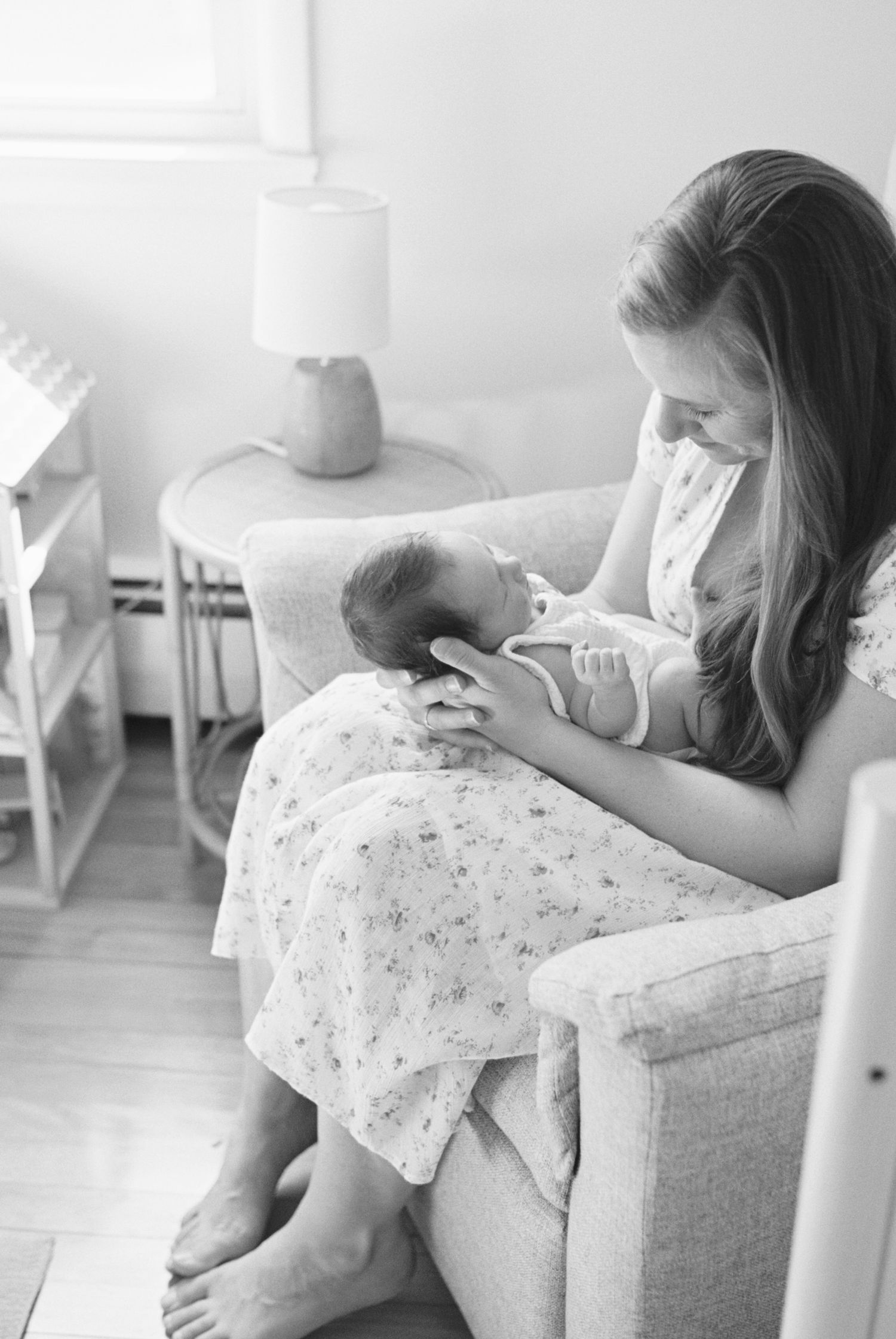 Mother in floral dress feeding newborn in cozy armchair.