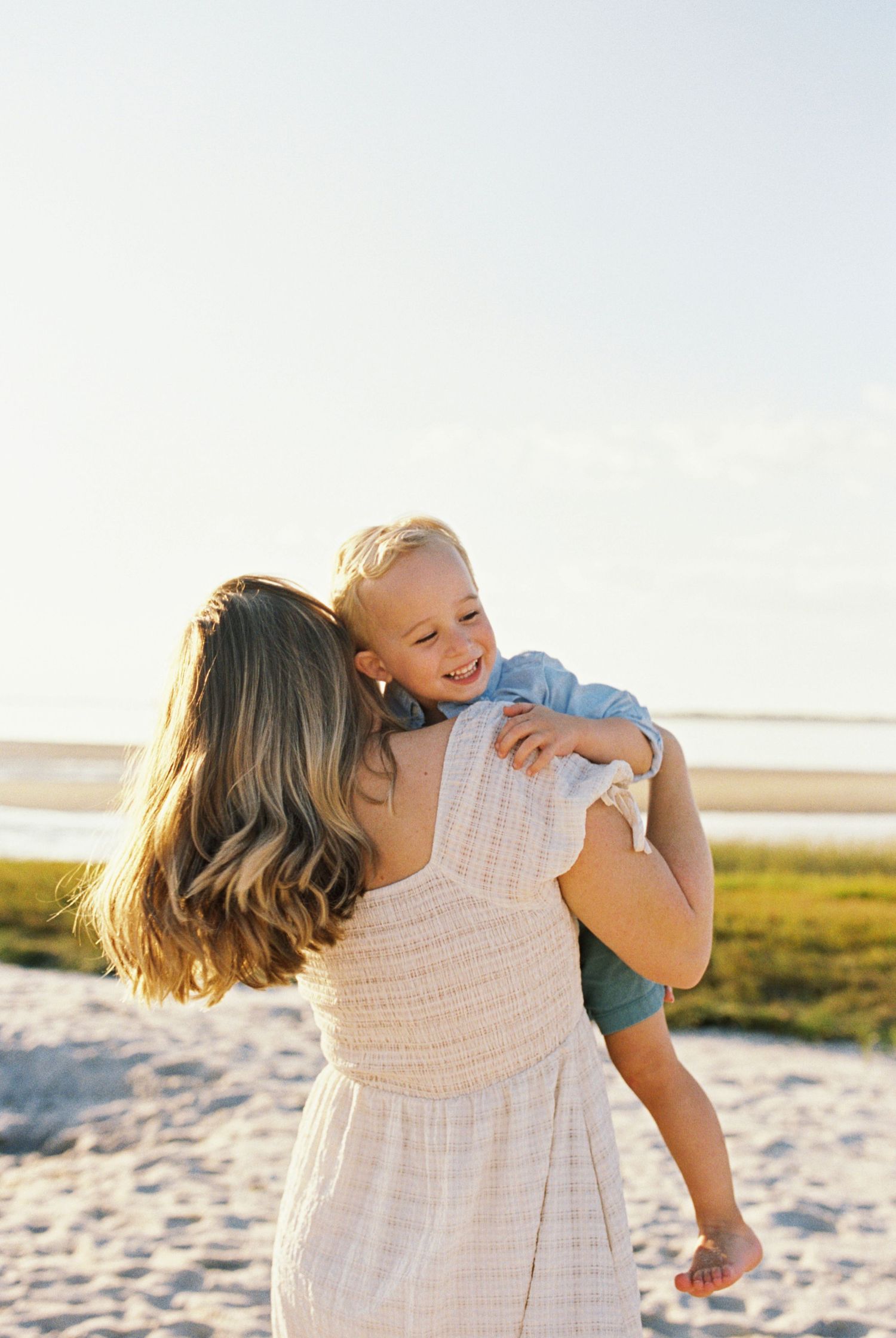A tender moment captured at sunset on a grassy beach with warm golden light illuminating the scene.