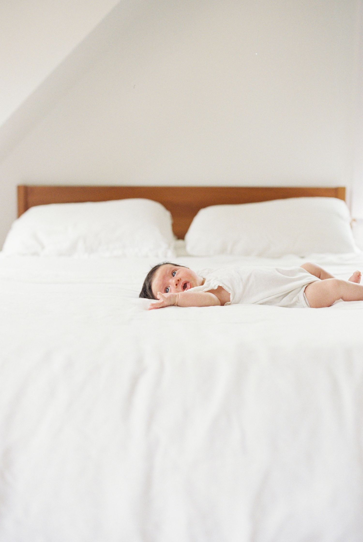 Baby lying peacefully on white bedding in a minimalist bedroom setting.