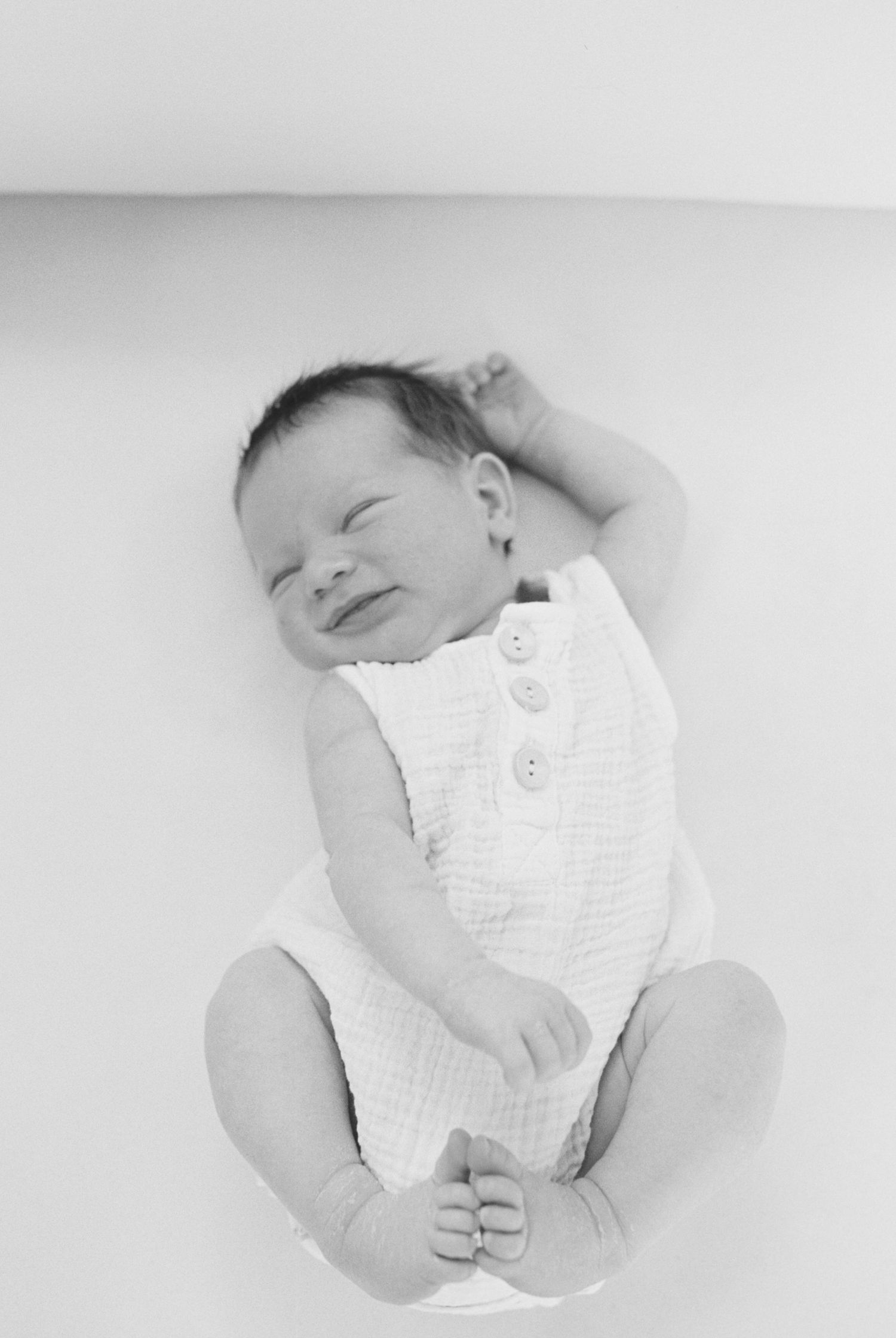 Overhead view of sleeping newborn baby in white clothing on white background.