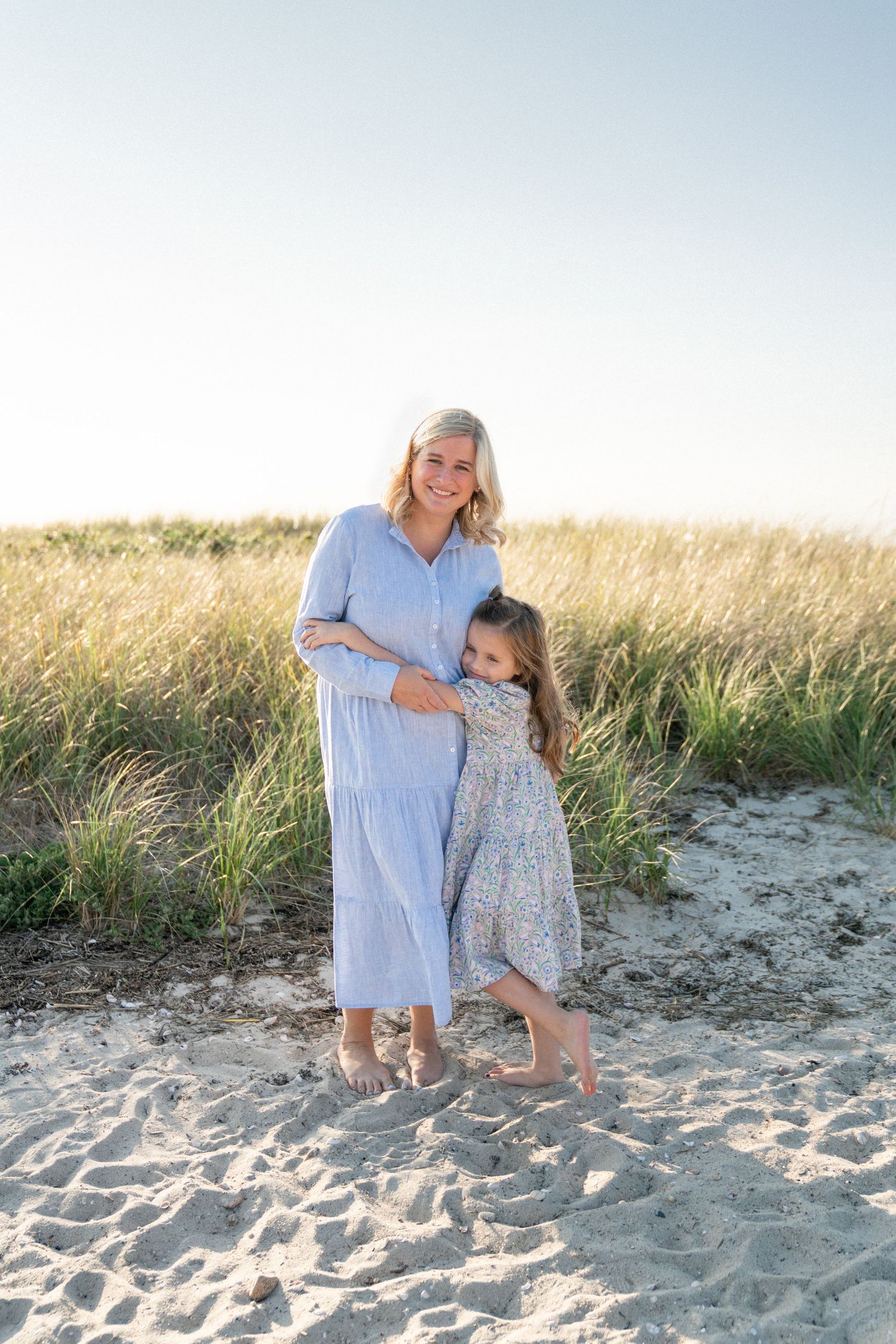 Mother and child playing together on a sandy beach in summer dresses.