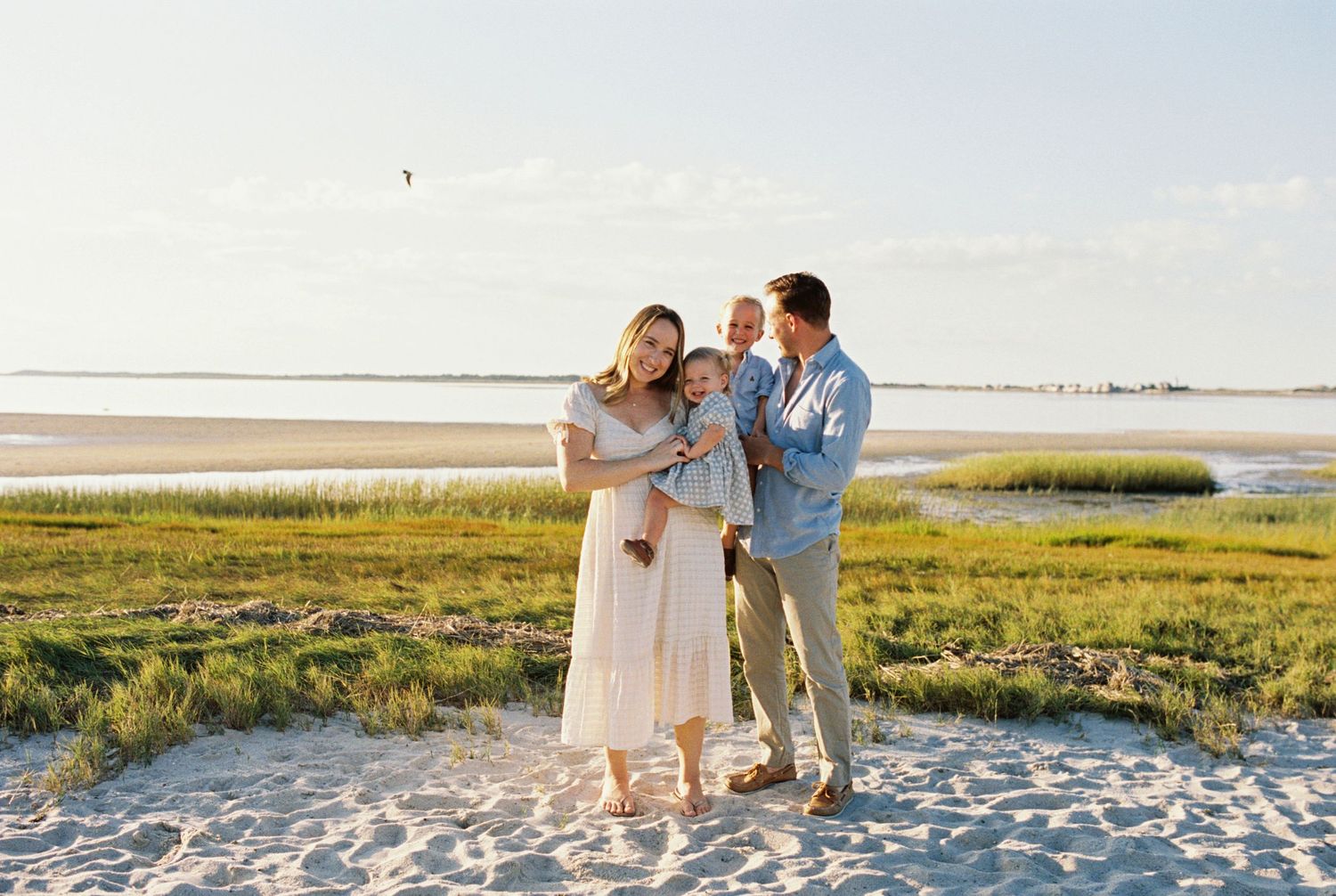 Beautiful beach photoshoot with family walking along coastal marshland at sunset.