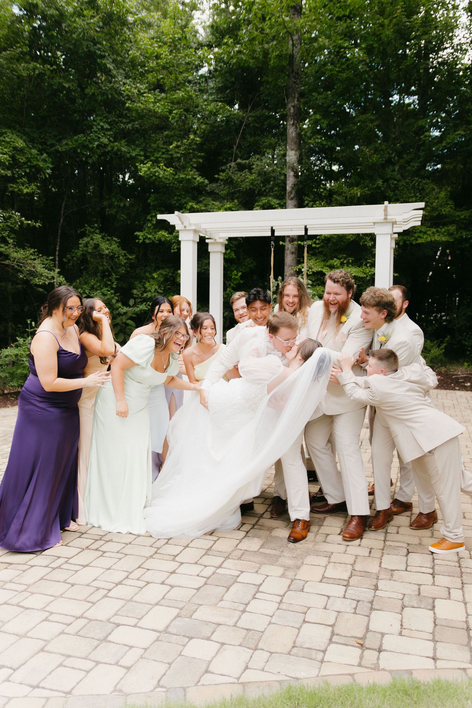 Wedding party poses playfully in a line on stone patio with white pergola in background. Commerce, Georgia wedding photographer.