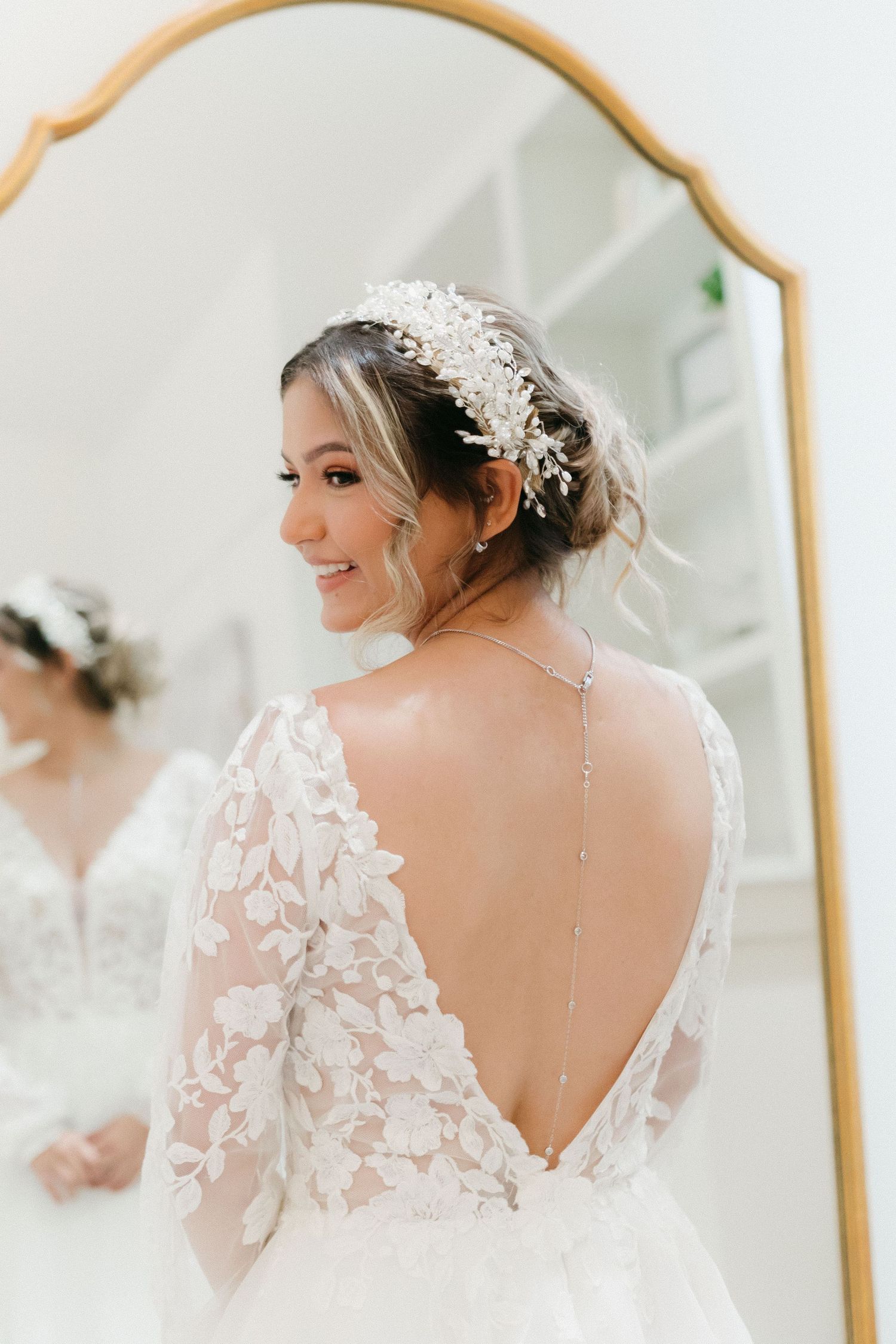 A delicate lace wedding gown with floral appliques and open back design catches light from nearby windows. Wedding photographer in Cumming.