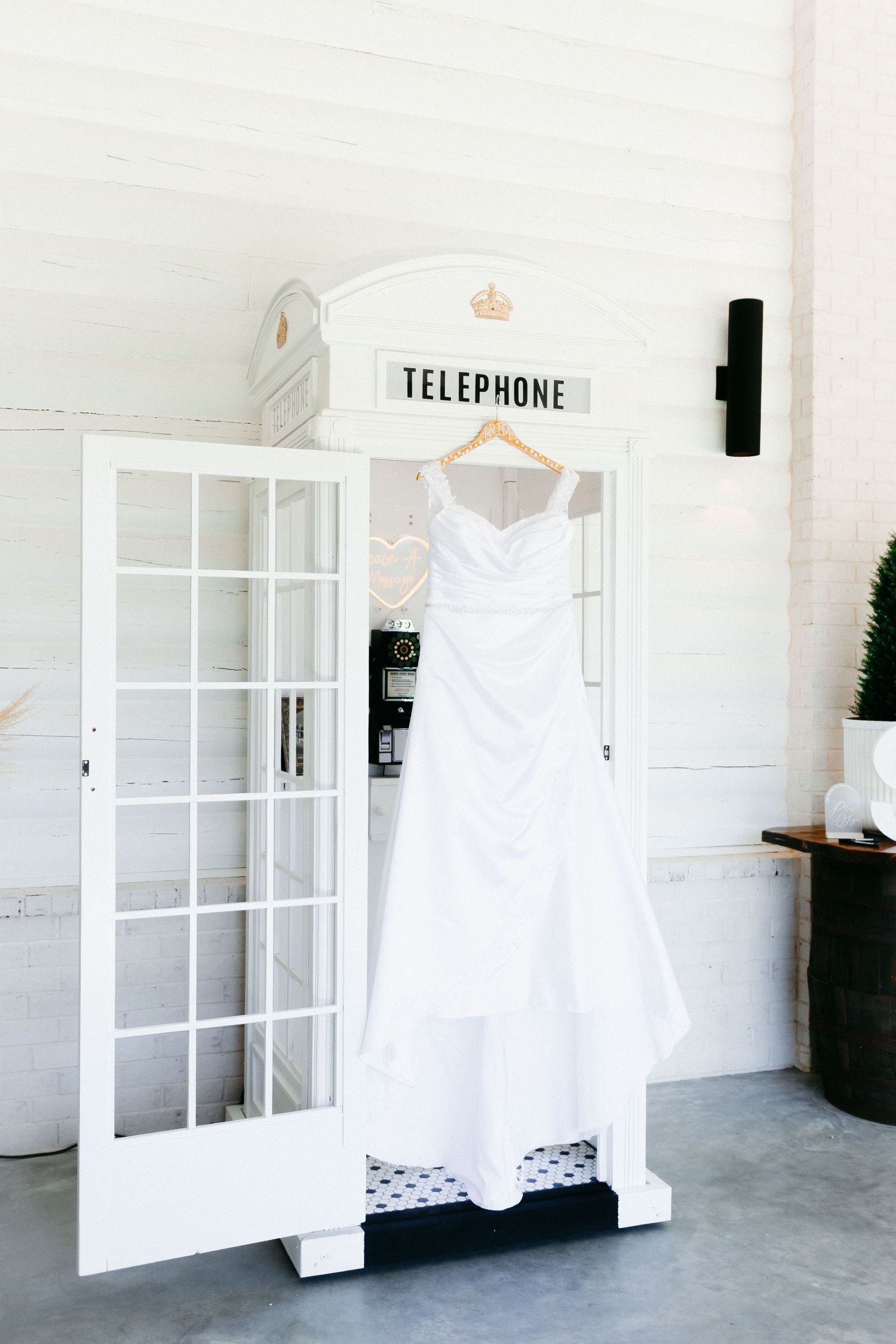 White wedding dresses hang on display against crisp white walls near a telephone booth. Wedding photographer in Clarkesville, Georgia.