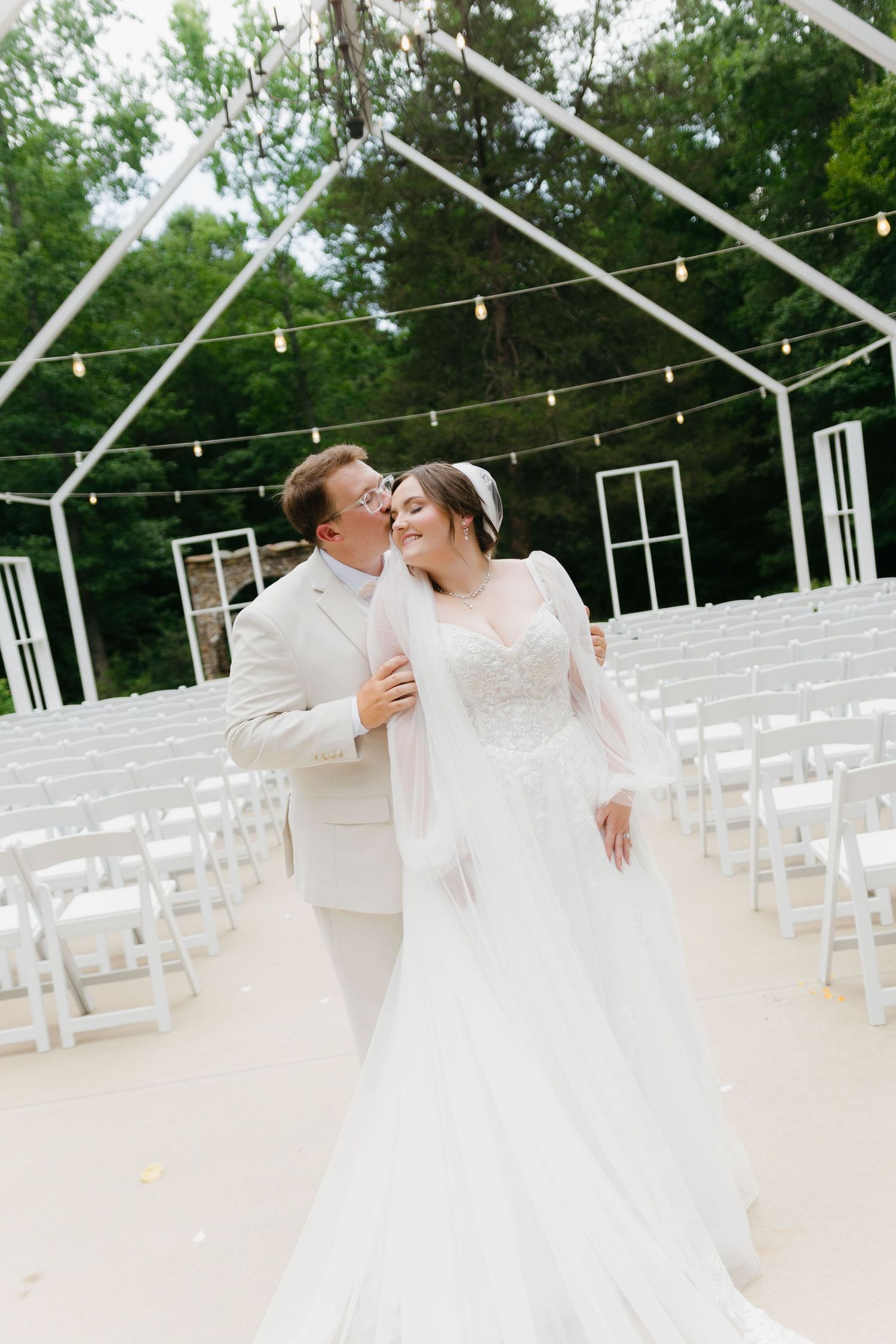 Outdoor wedding ceremony setup with white chairs and string lights under clear tent. Commerce, Georgia wedding photographer.