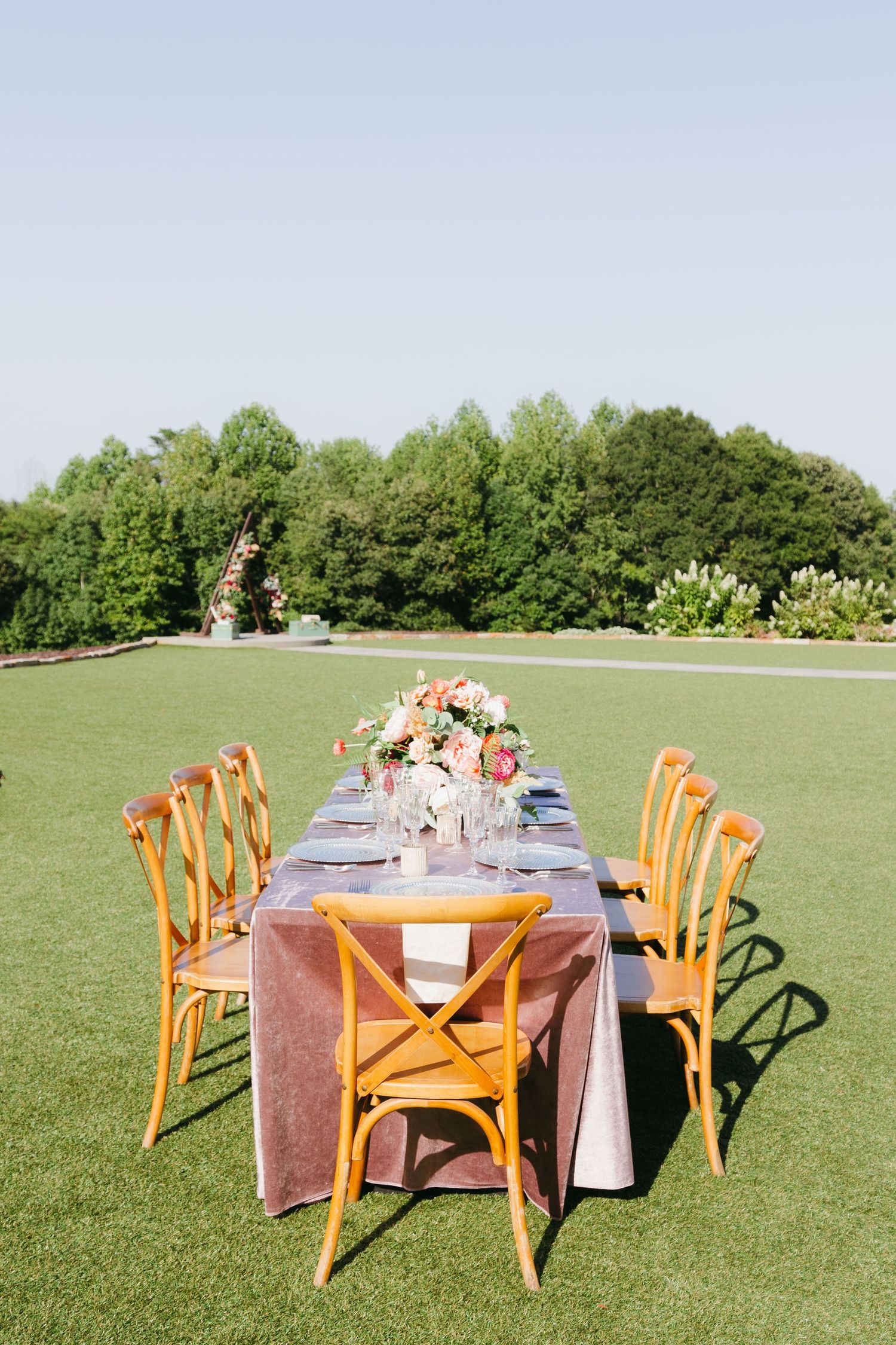 Outdoor wedding reception setup with wooden chairs and tables on a grassy field surrounded by trees. Luxury wedding photographer Georgia.