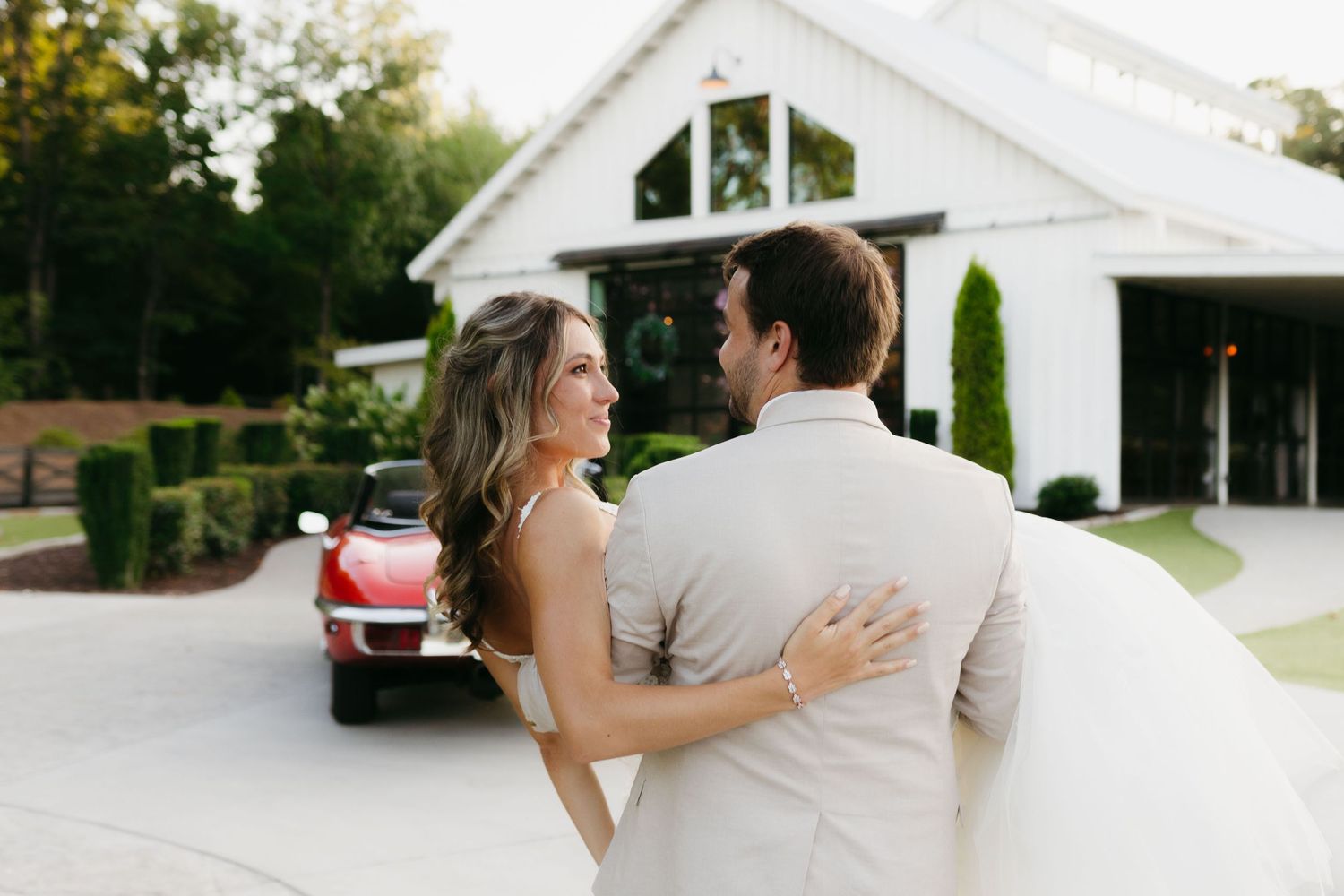 Newlyweds embrace in front of Meadows at Mossy Creek with vintage red car in background. Wedding photographer in Cleveland, Georgia.
