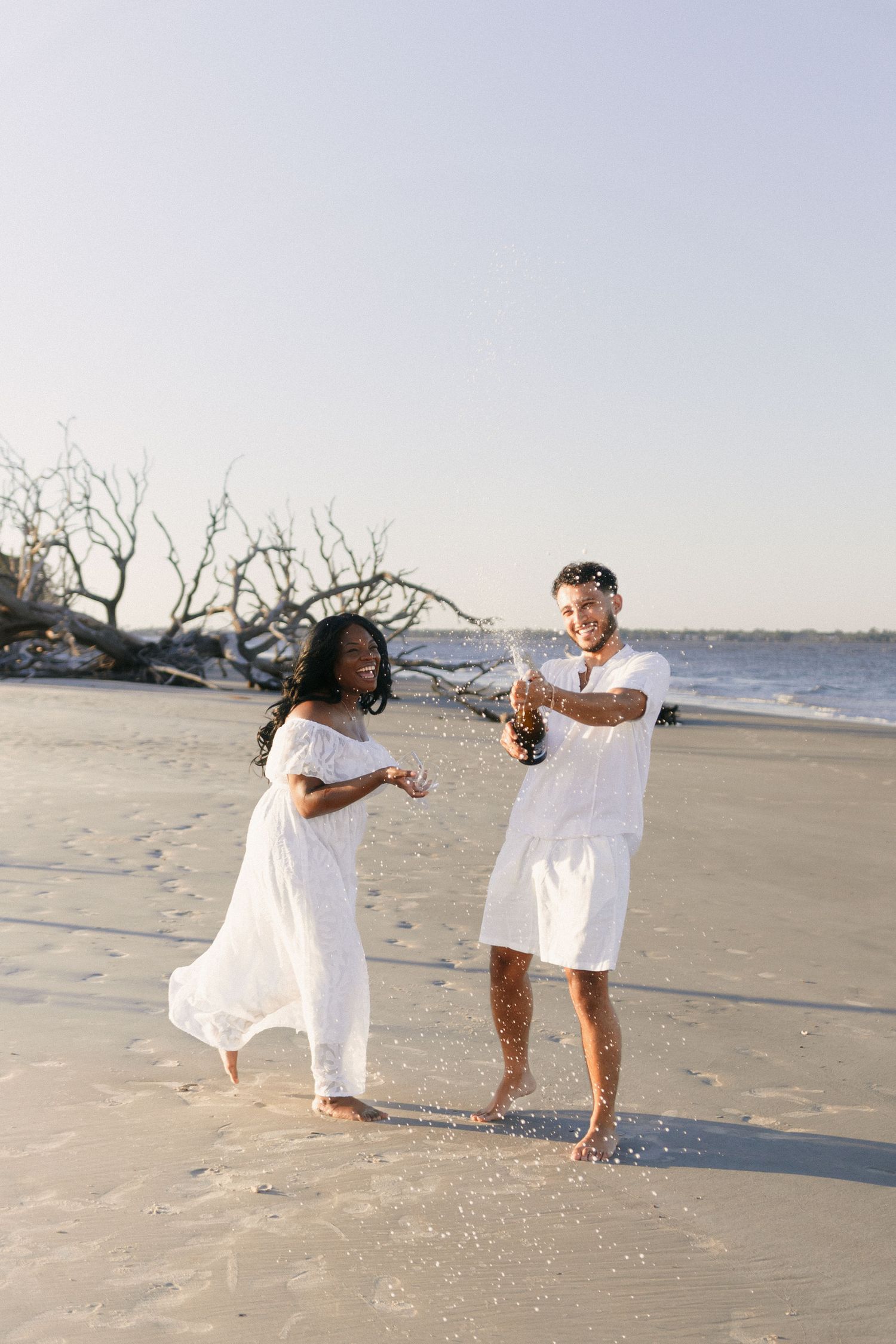 Two people in white outfits play and splash in the surf at a beach during sunset. Jekyll island elopement photographer.