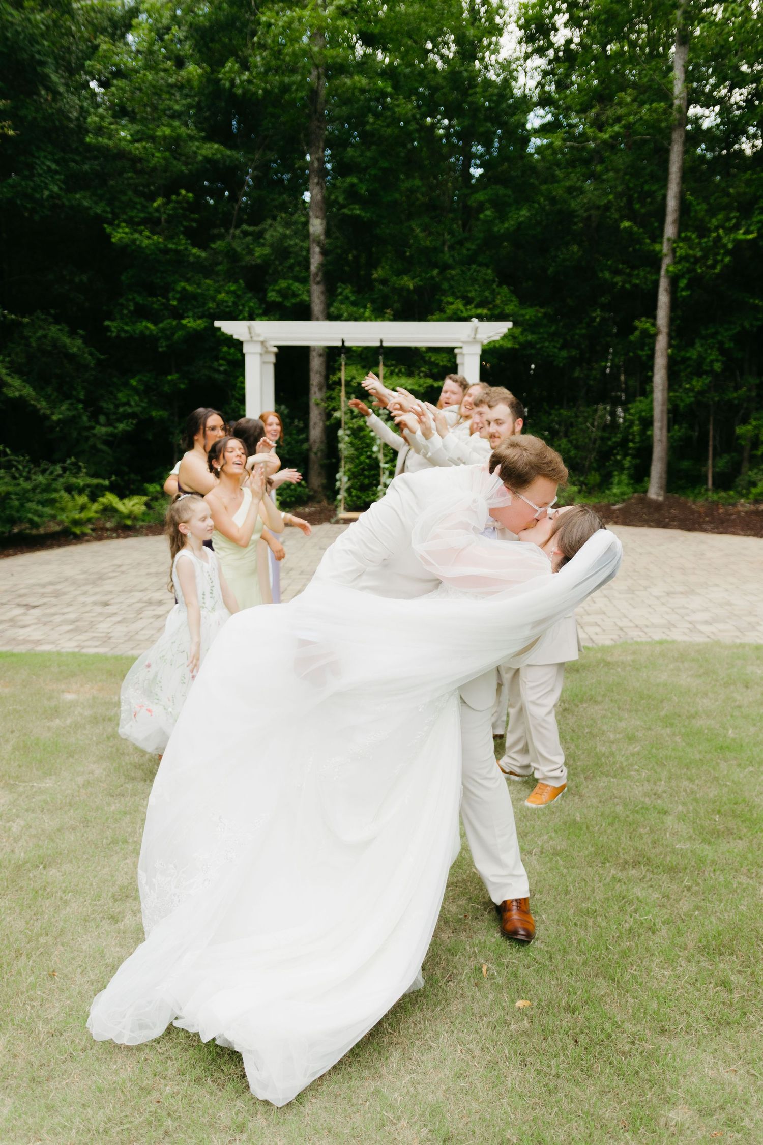 Energetic wedding party photo with dramatic dress toss in front of white pergola. Commerce, Georgia wedding photographer.