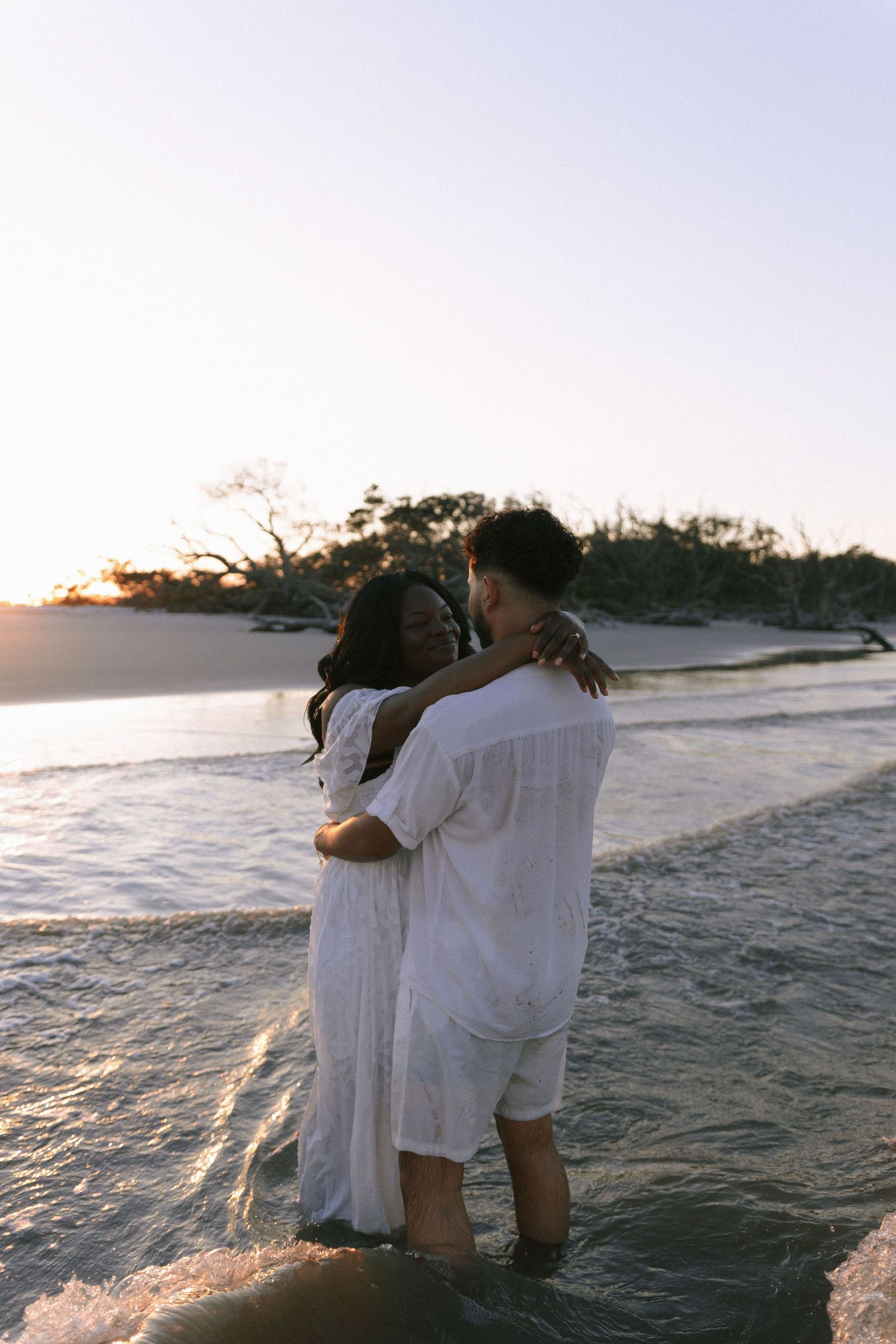 Couple embraces while standing in ocean waves during sunset beach photoshoot. Jekyll island elopement photographer.