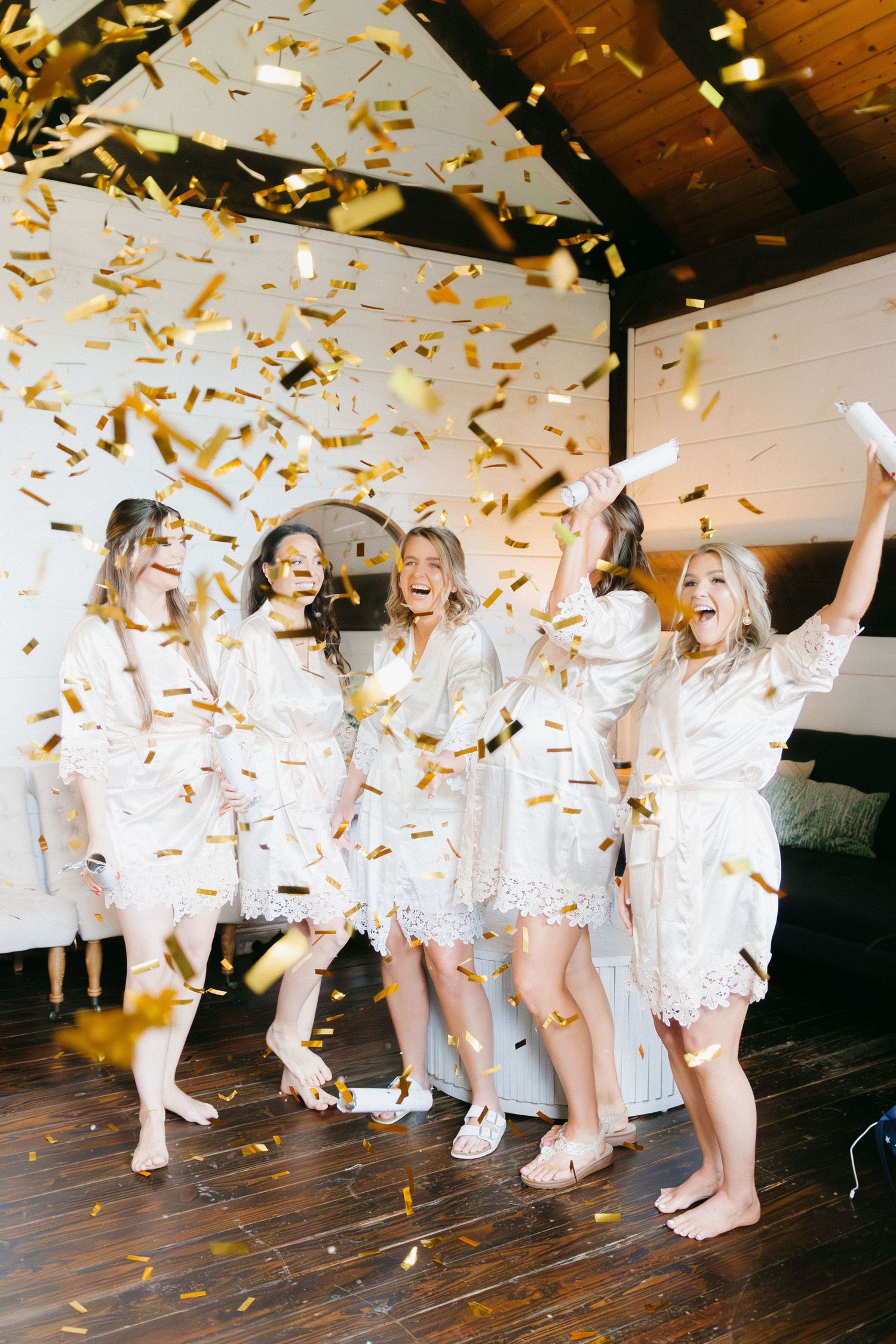 Wedding party celebrating with gold confetti while wearing white outfits on wooden floor. Dahlonega, Georgia wedding photographer.