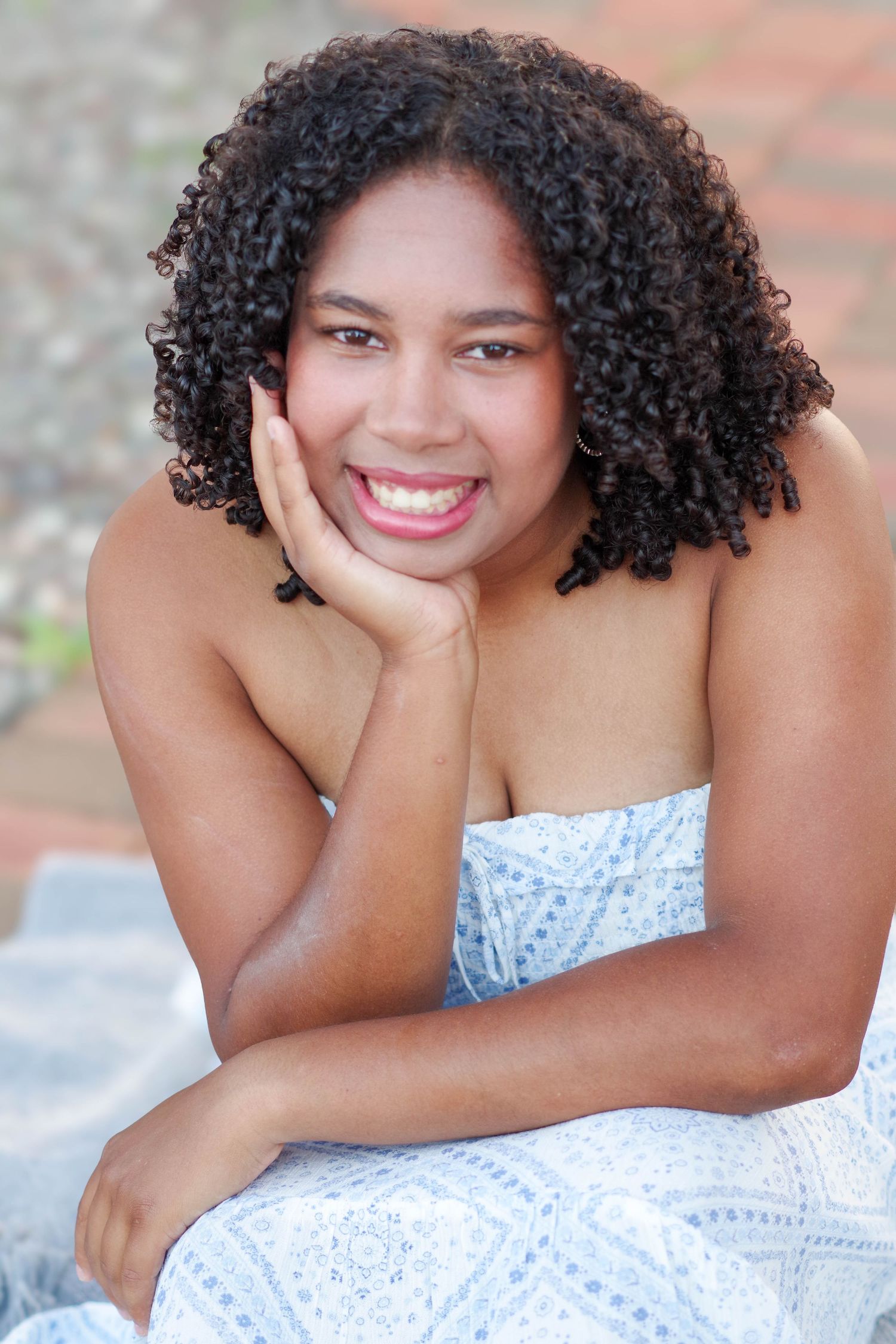 Close-up portrait of someone in white dress with natural curls smiling at camera.