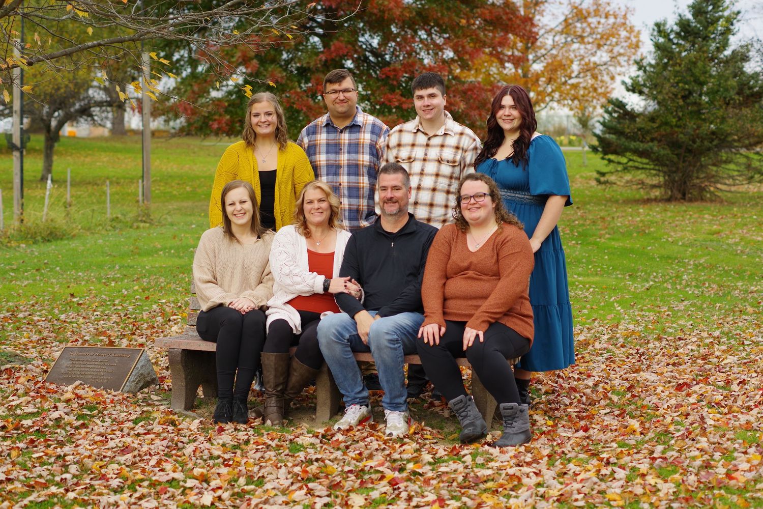 Family portrait outdoors with fall colors and leaves scattered on grassy ground.