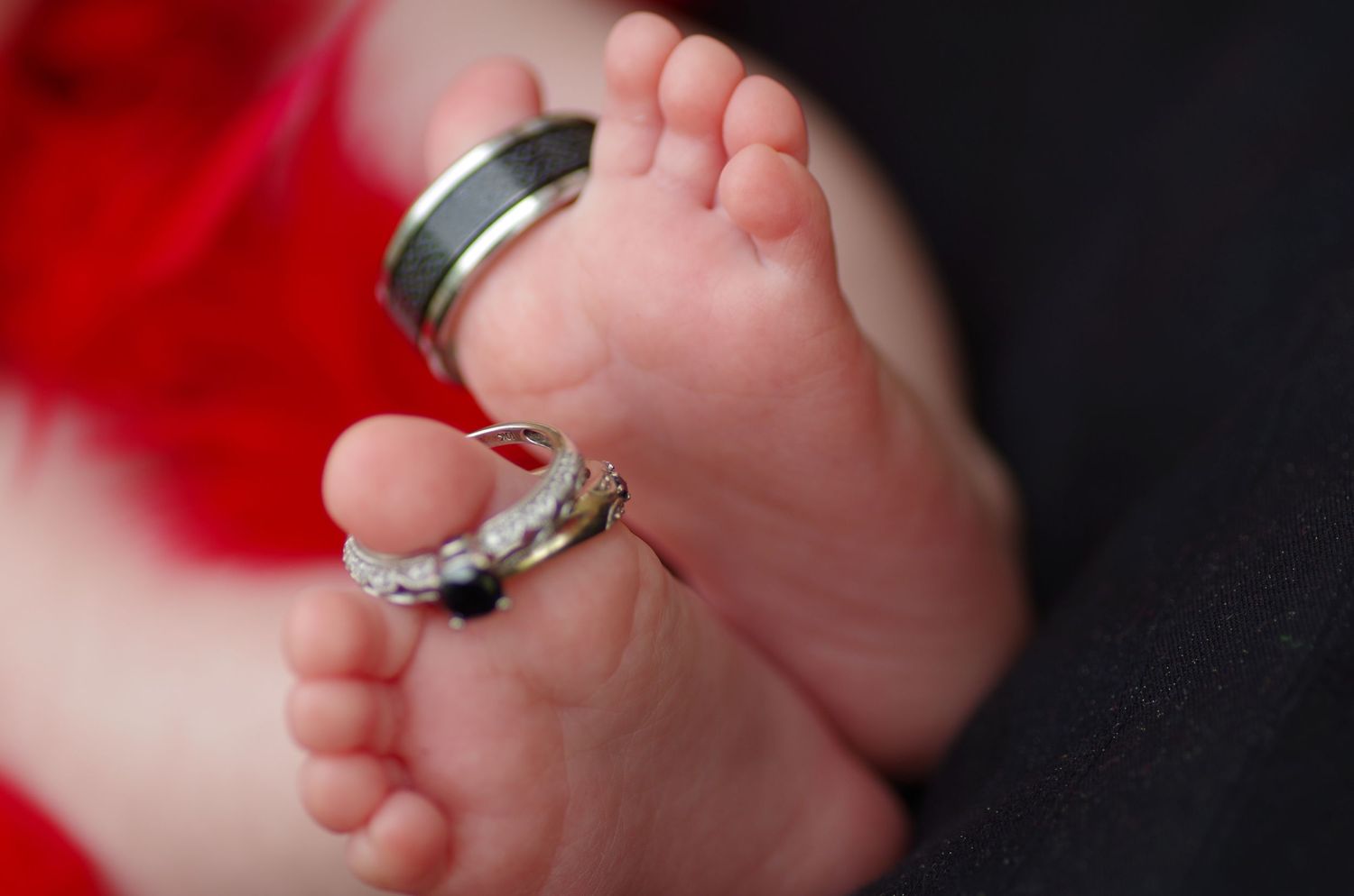 Wedding rings placed on tiny baby feet against red background.