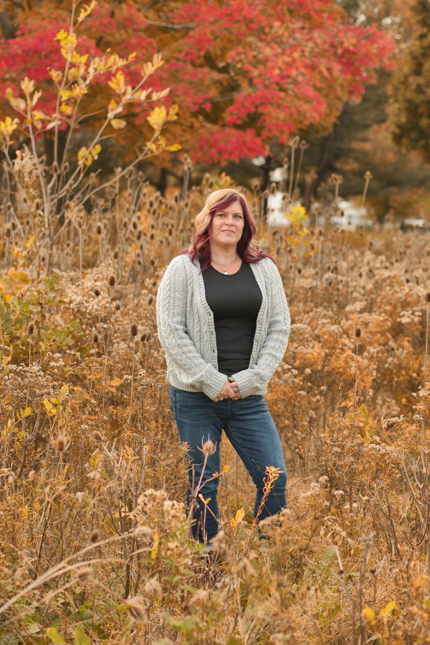 Autumn outdoor portrait with gray cardigan against backdrop of red and gold fall foliage.