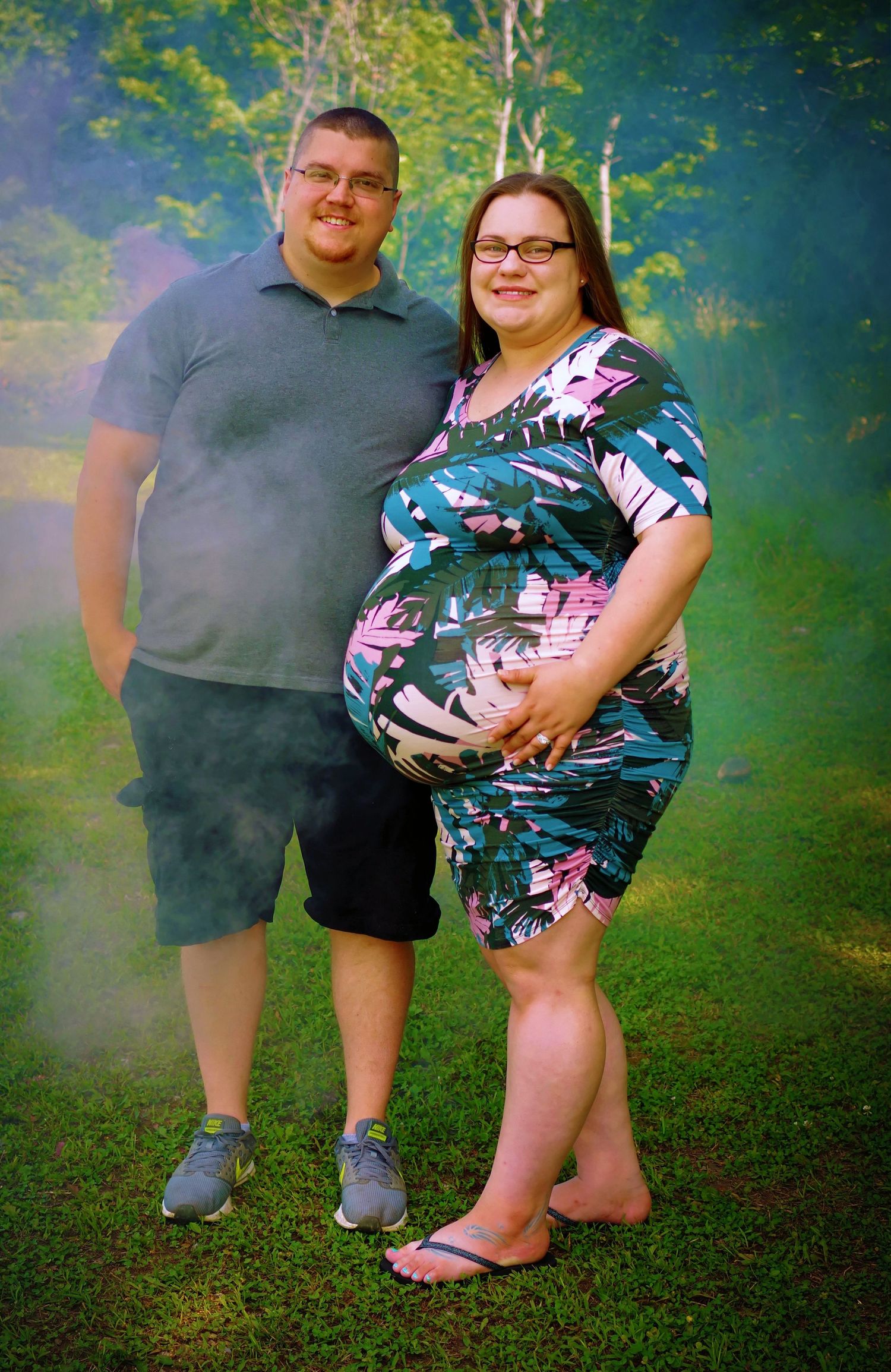 Expectant couple posing barefoot on grass with floral maternity dress.