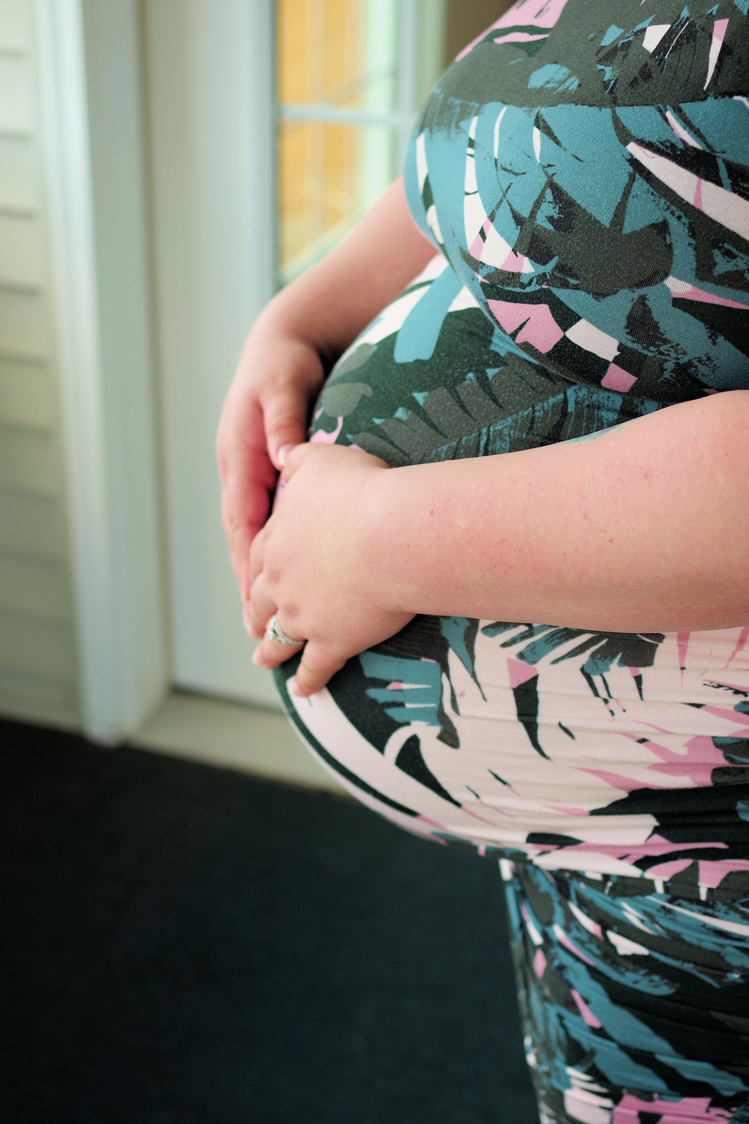 Maternity photo detail showing hands cradling pregnant belly in patterned dress.