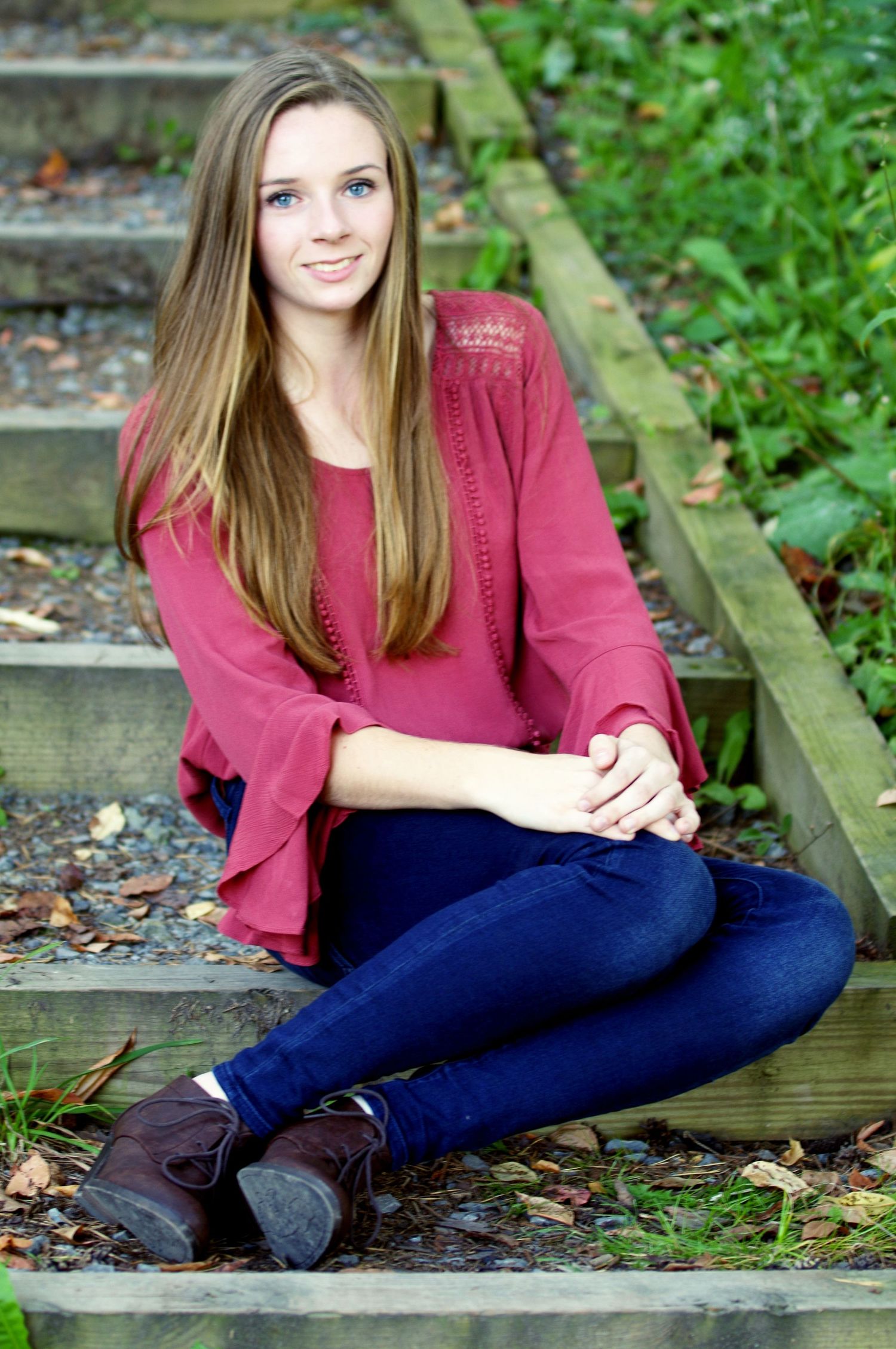 Senior photo session on wooden steps surrounded by greenery.