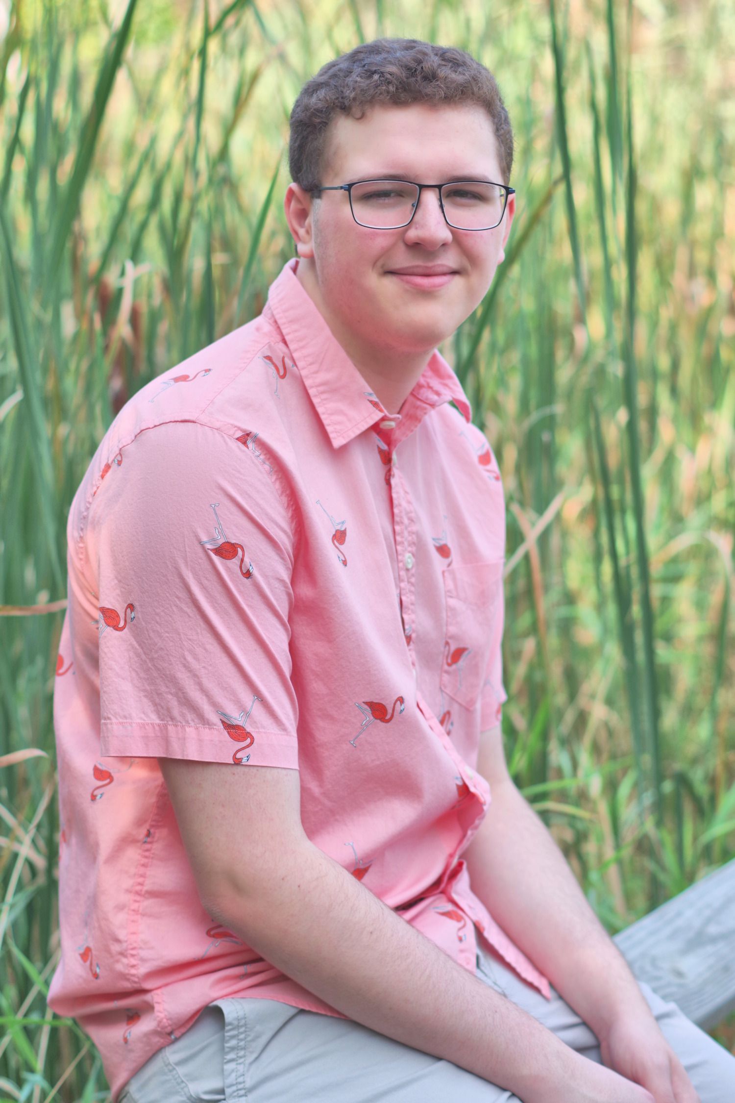 Summer portrait in a pink patterned shirt against tall grass backdrop.