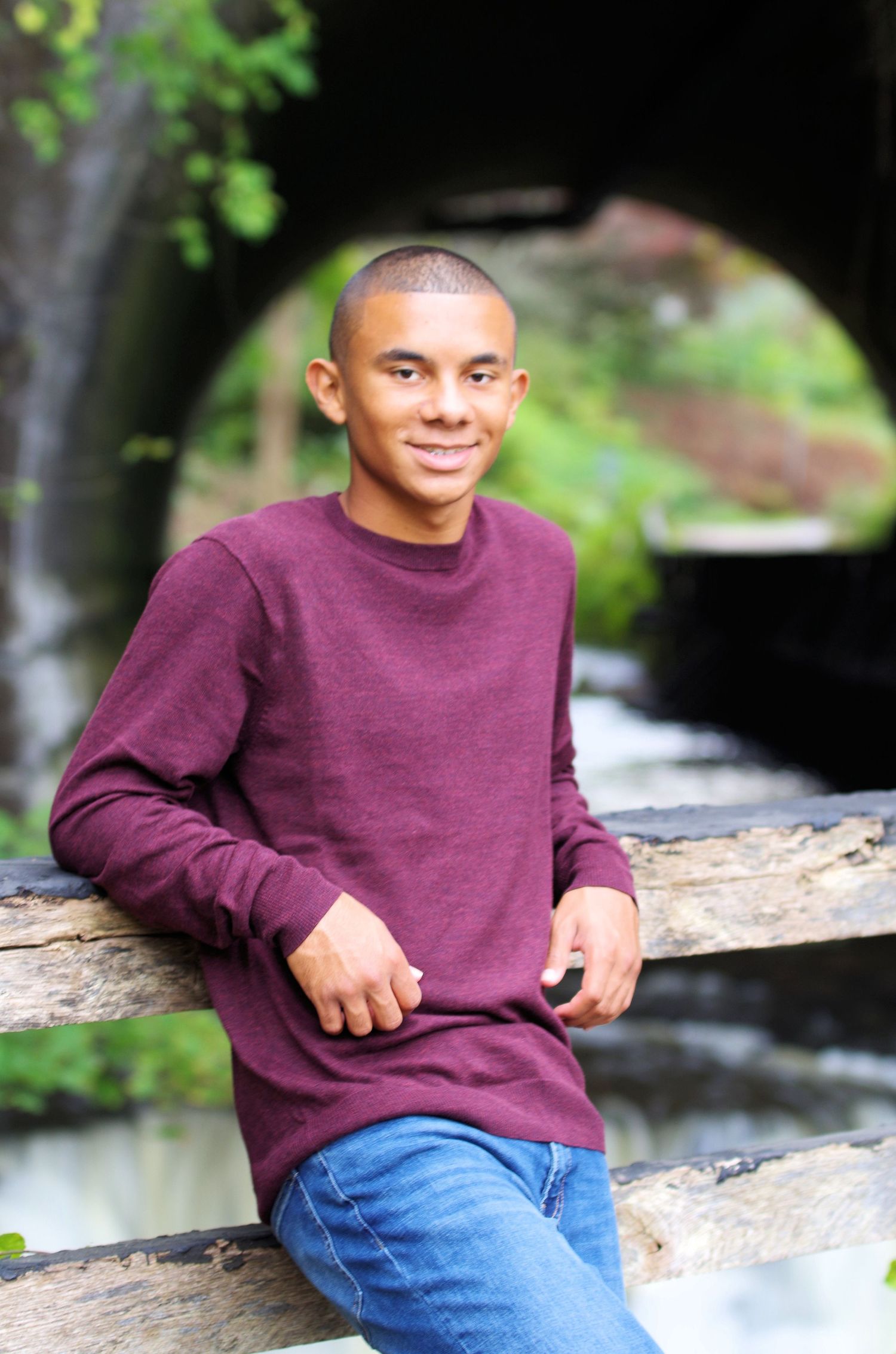 Casual outdoor portrait on wooden railing with burgundy sweater and jeans.