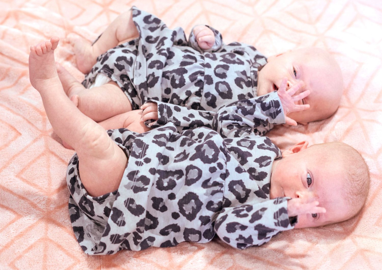 Baby in leopard print dress lying on pink blanket.