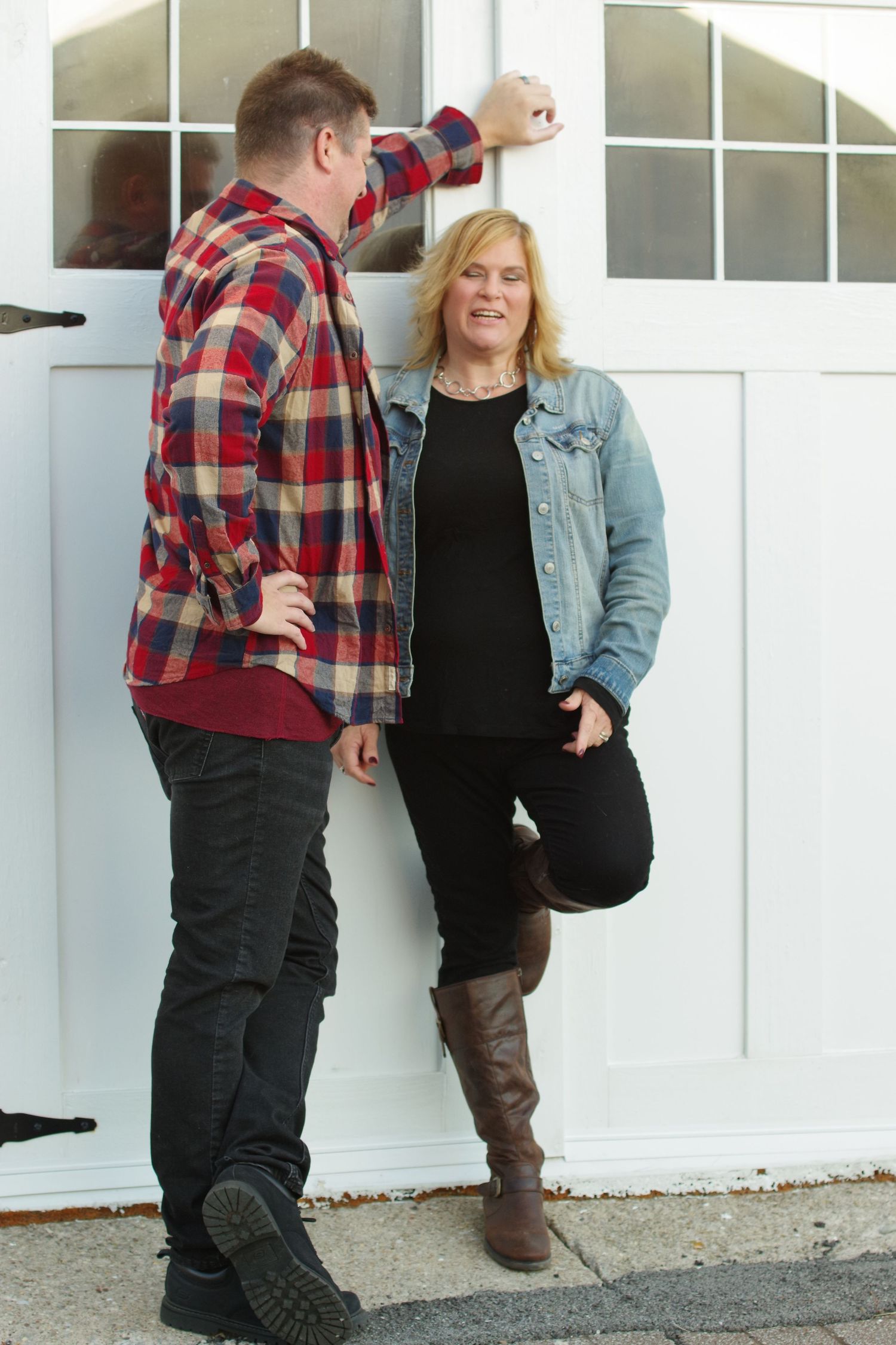 Casual couple poses by white garage door, wearing plaid and denim.