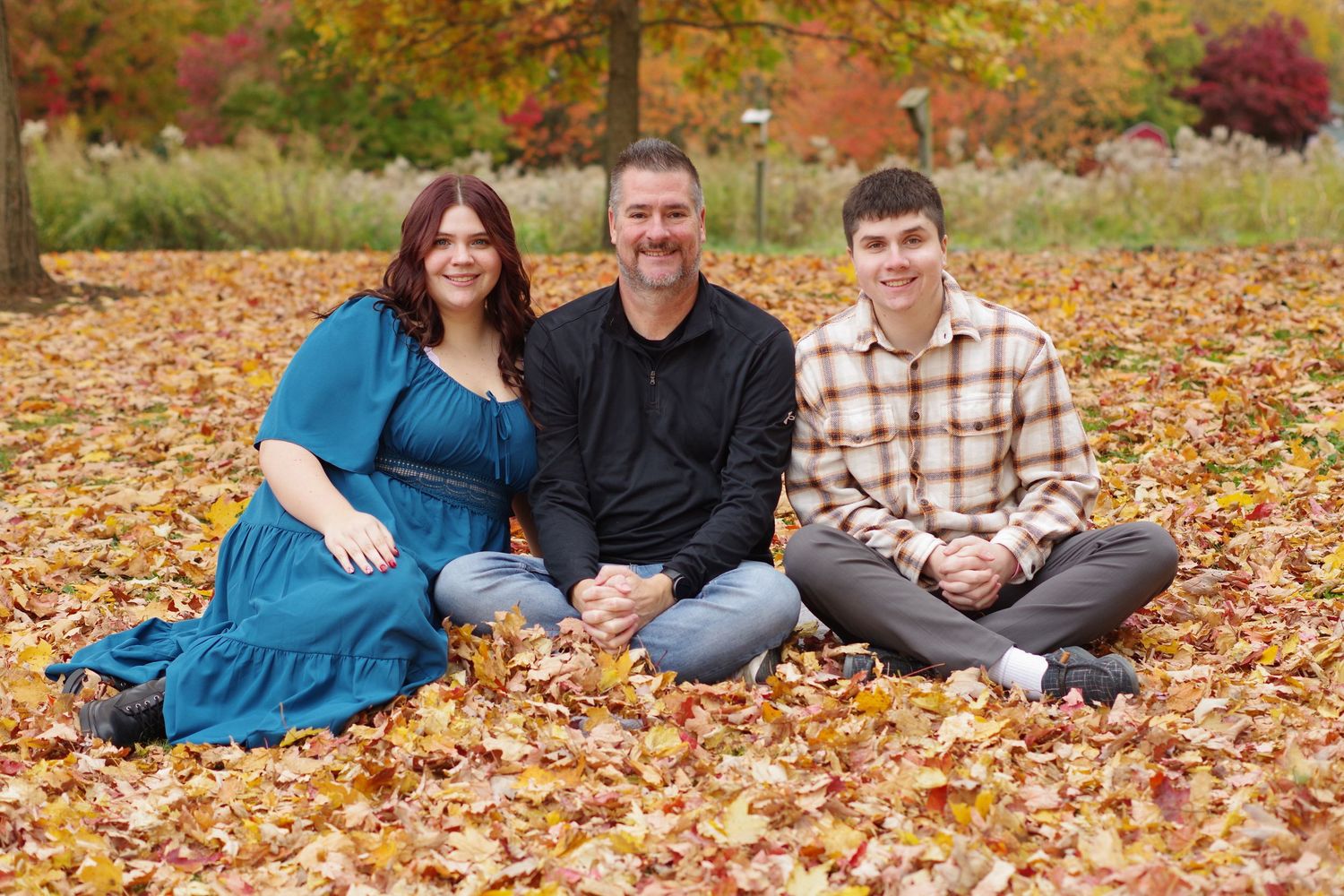 Small group seated on ground covered in fallen autumn leaves during photo session.