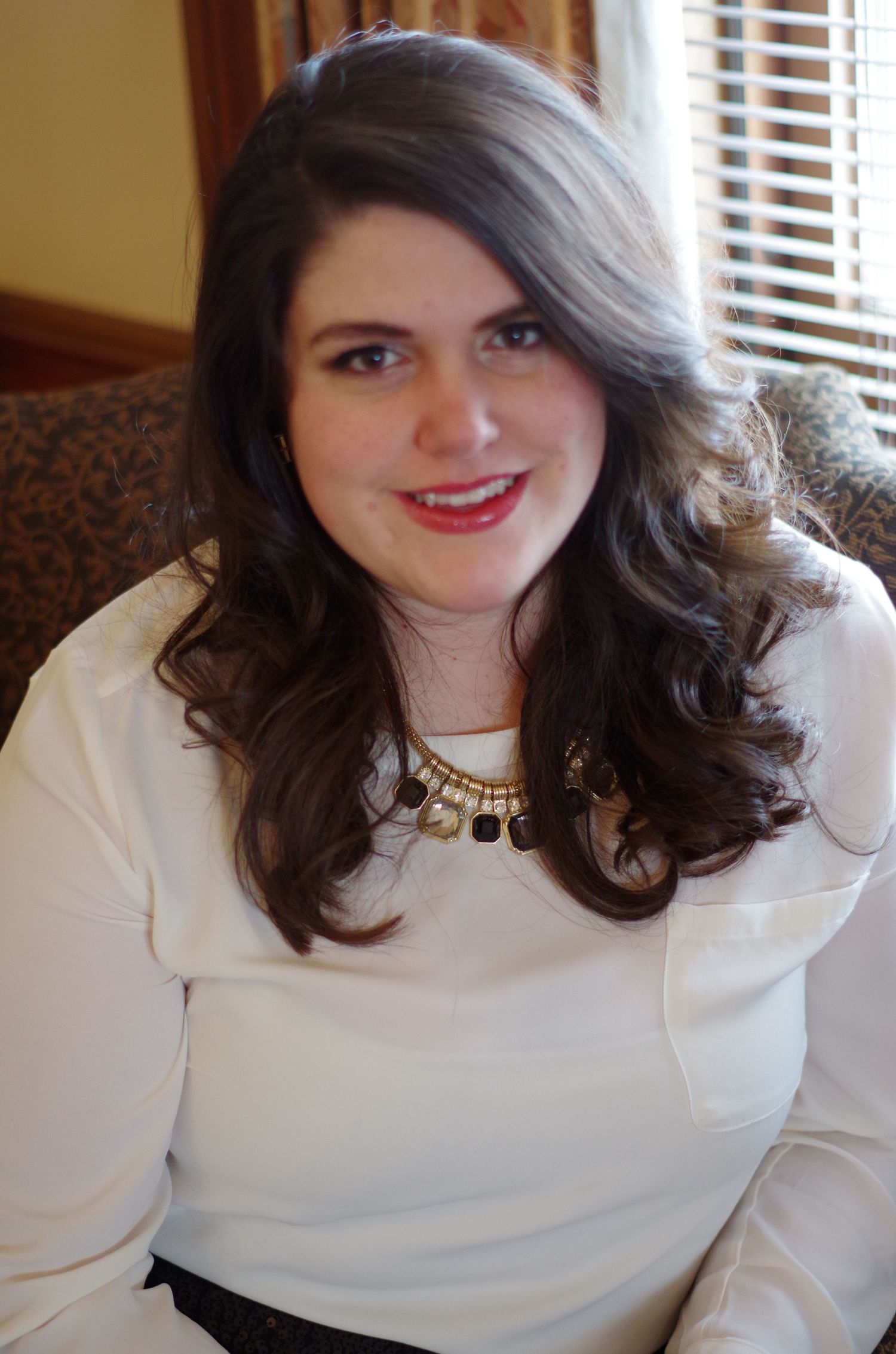 A person wearing a white sweater smiles warmly in an indoor setting.