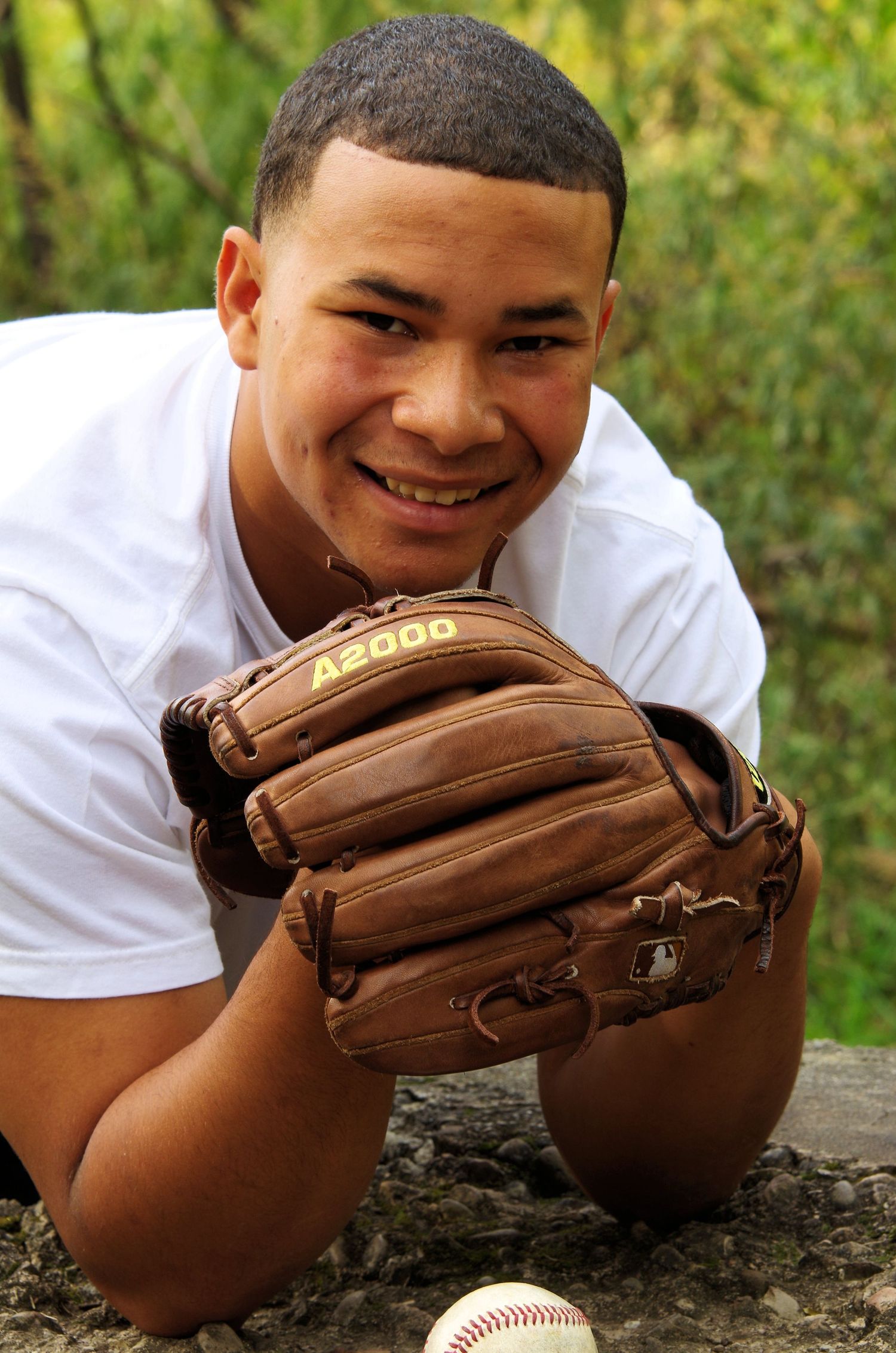 Baseball player posing with brown leather glove and baseball on stone surface.