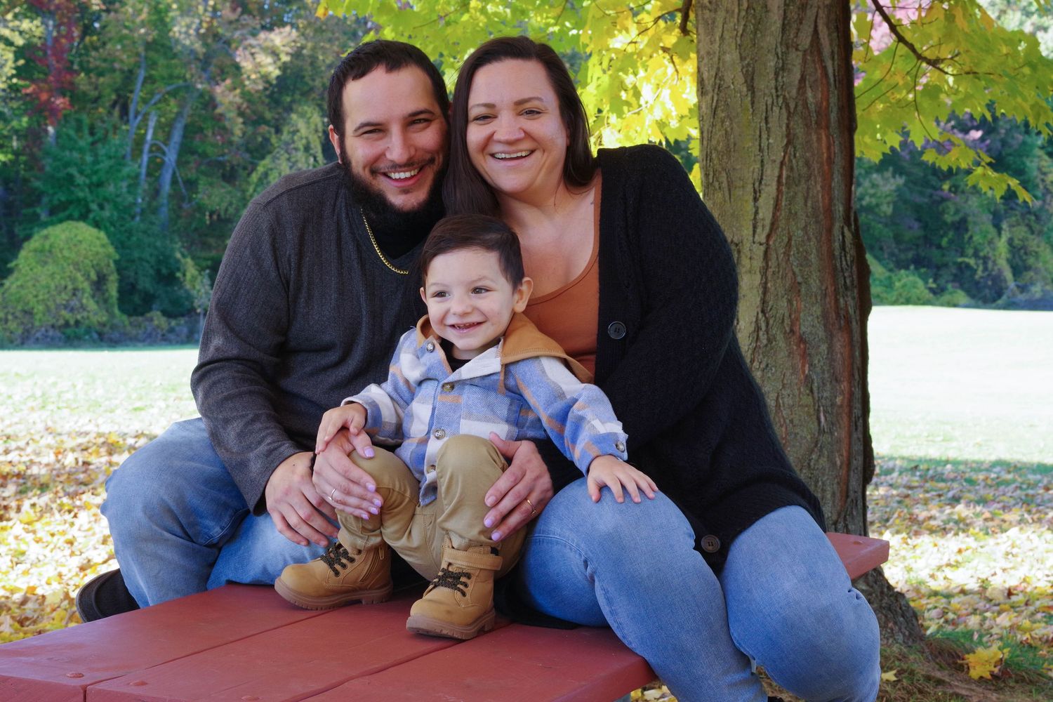 Small family seated together on red bench during autumn photo session.