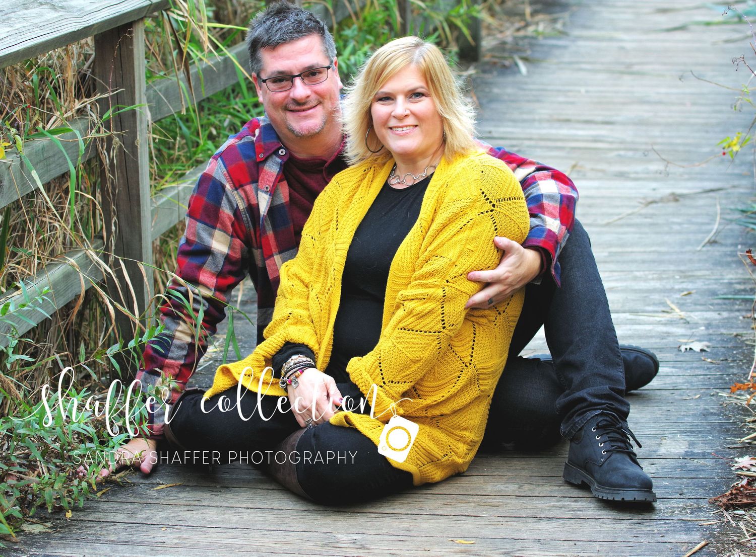 A couple sits together on a wooden boardwalk, with one wearing a bright yellow sweater.
