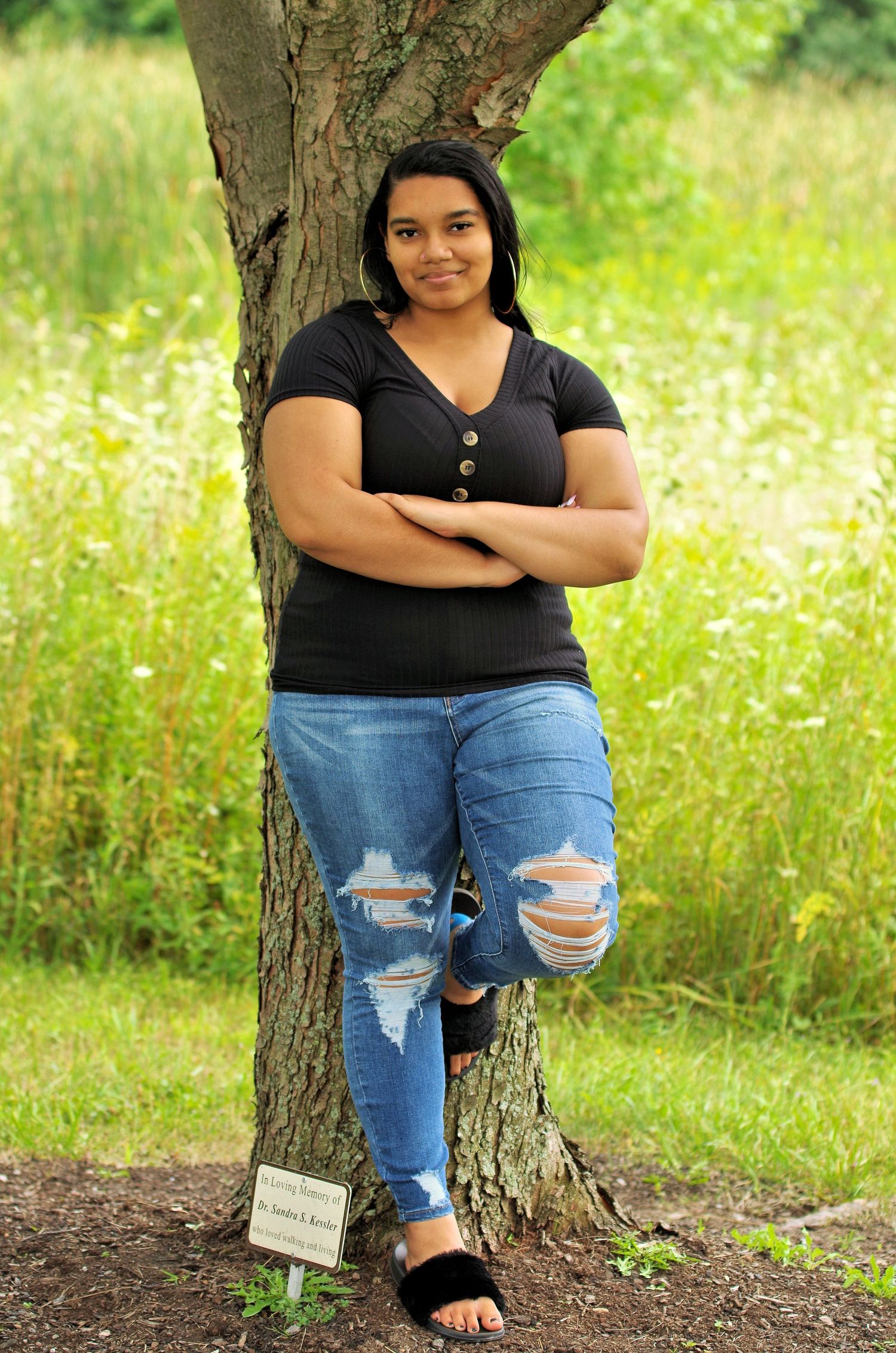 A casual outdoor portrait against a tree trunk with wildflowers in the background.