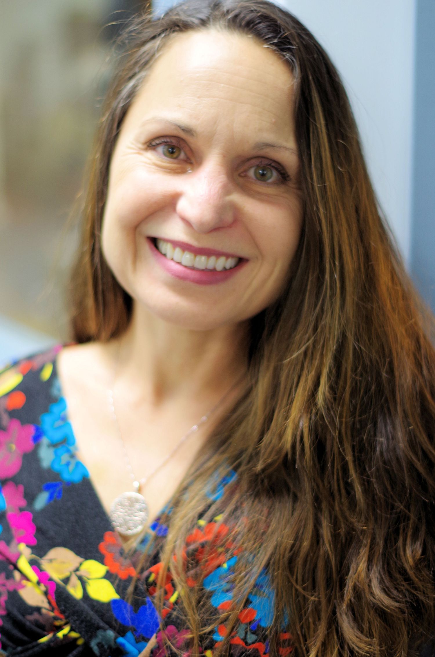 Close-up shot of someone in a vibrant floral print dress with long brown hair against a blurred background.