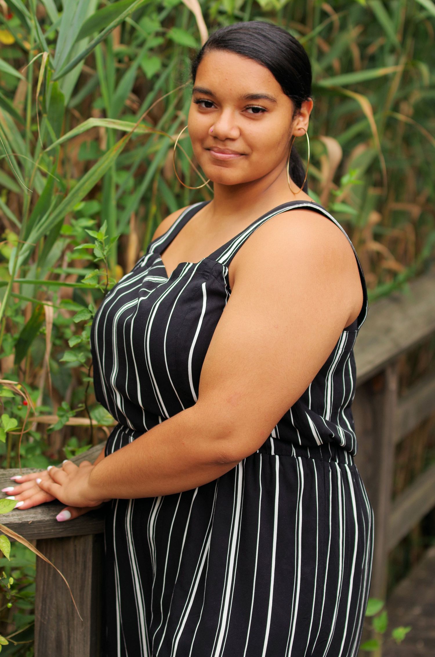 A portrait in a black and white striped dress against a natural green backdrop.