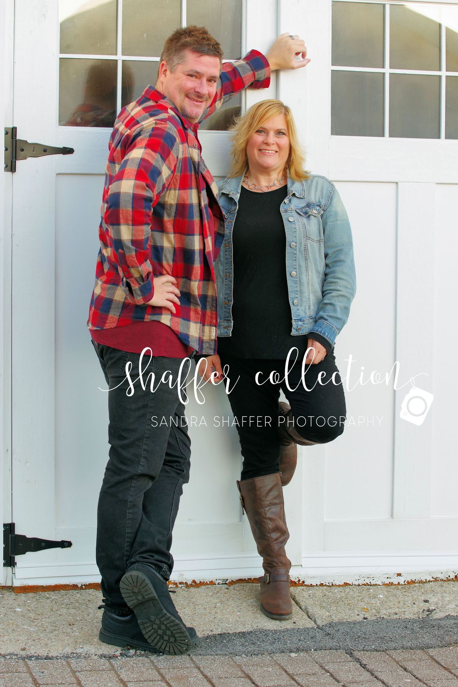 A couple poses casually by a white door wearing coordinating plaid and denim outfits.