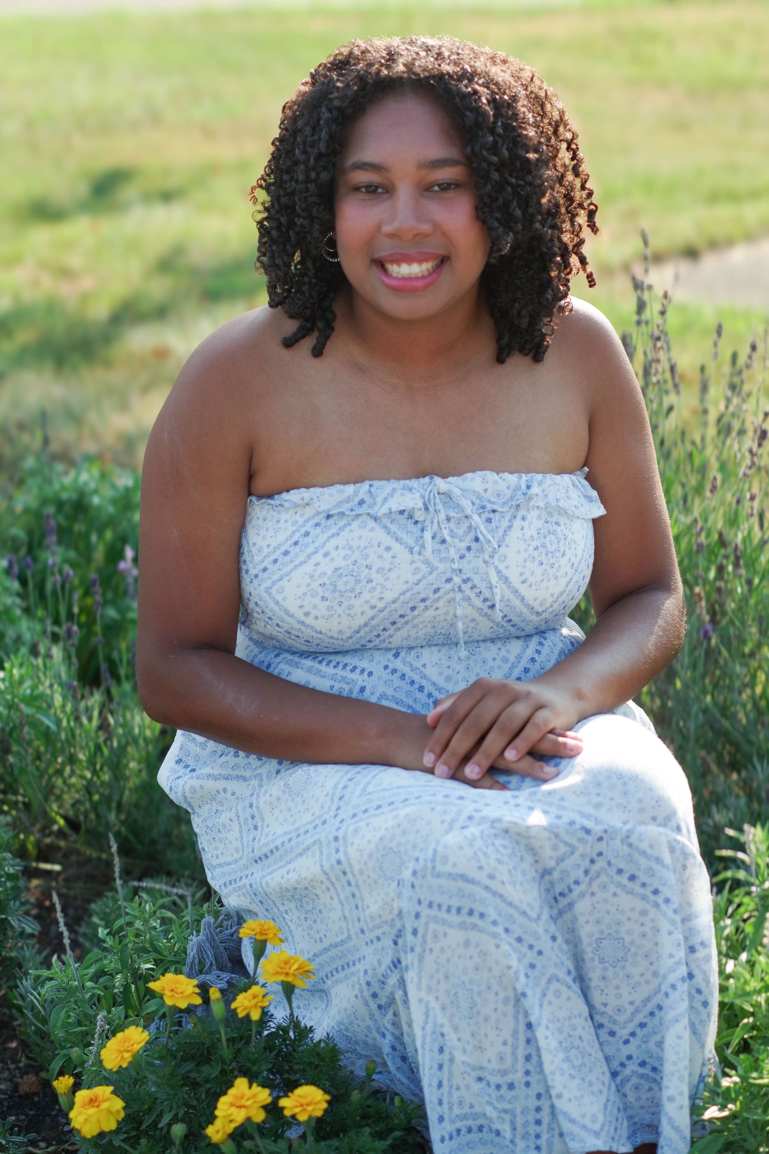 Summer portrait of woman in white dress sitting among yellow flowers.