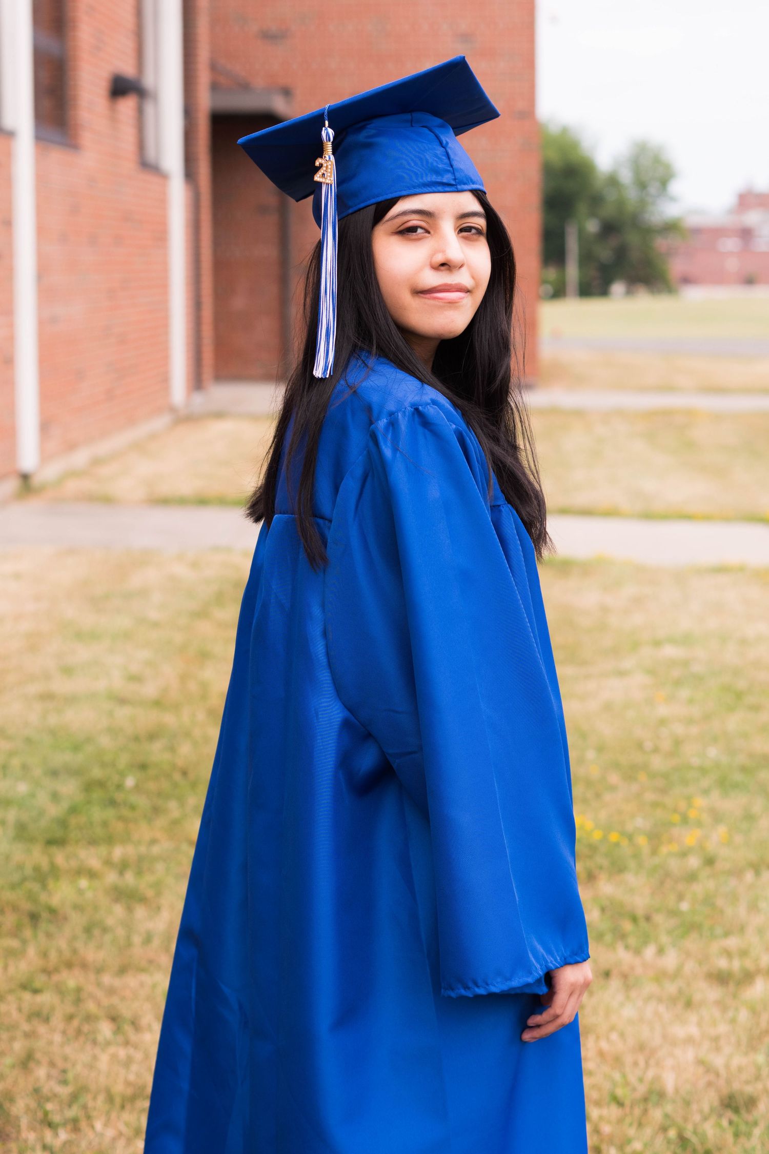 Side profile of graduate in blue regalia standing against brick building backdrop.
