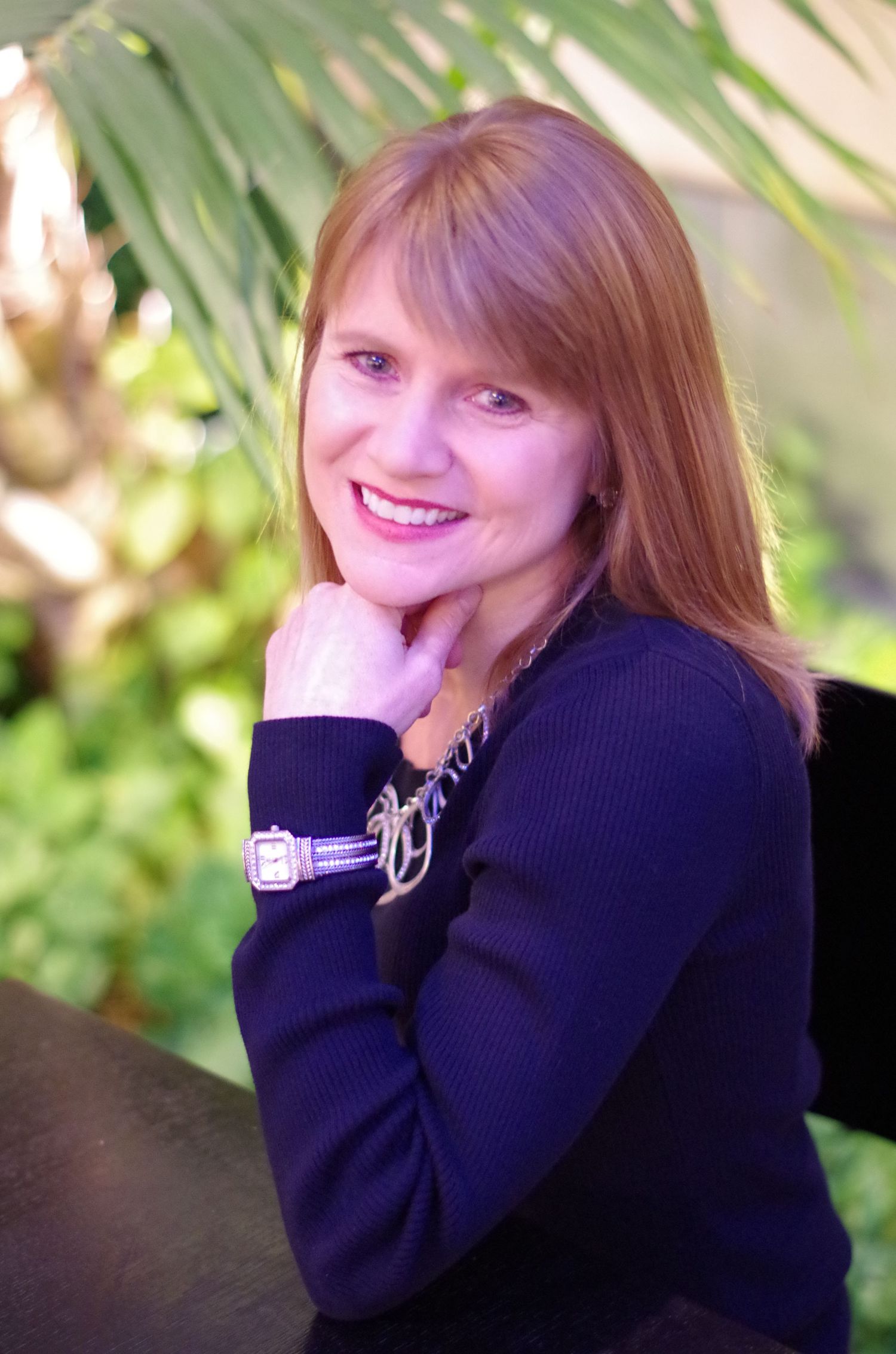 Casual outdoor portrait with navy sweater and watch against tropical foliage background.