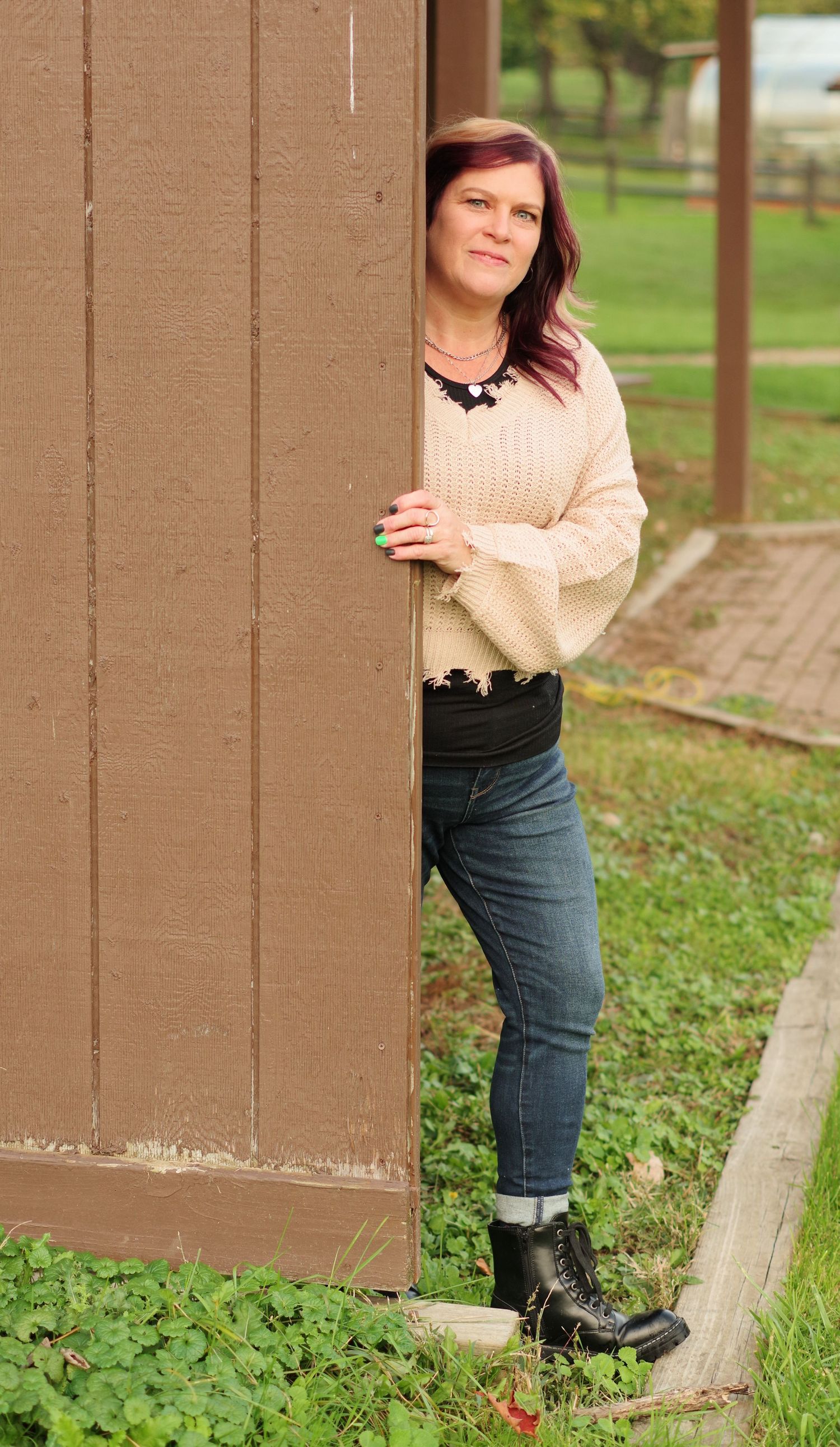 Person in cream sweater and boots poses playfully beside brown wooden post.