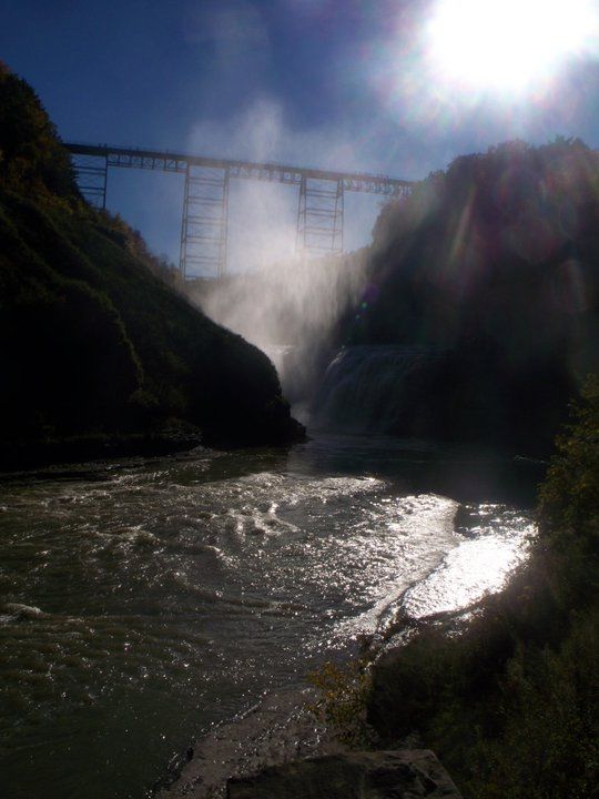 Sunlight streams over a dramatic dam releasing water through a rocky gorge.