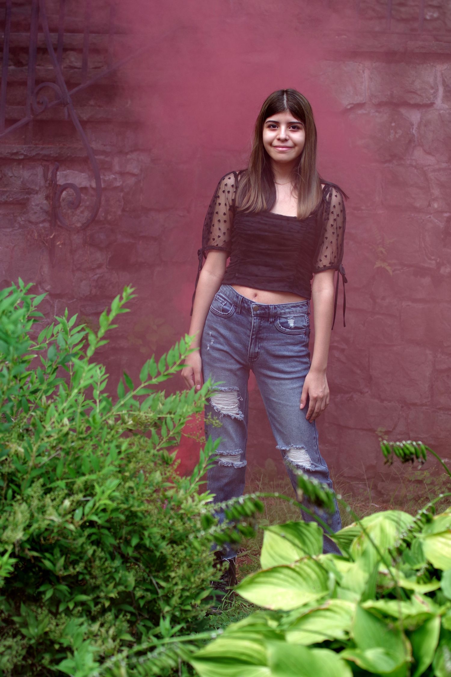 Portrait against brick wall with lush green plants in foreground.