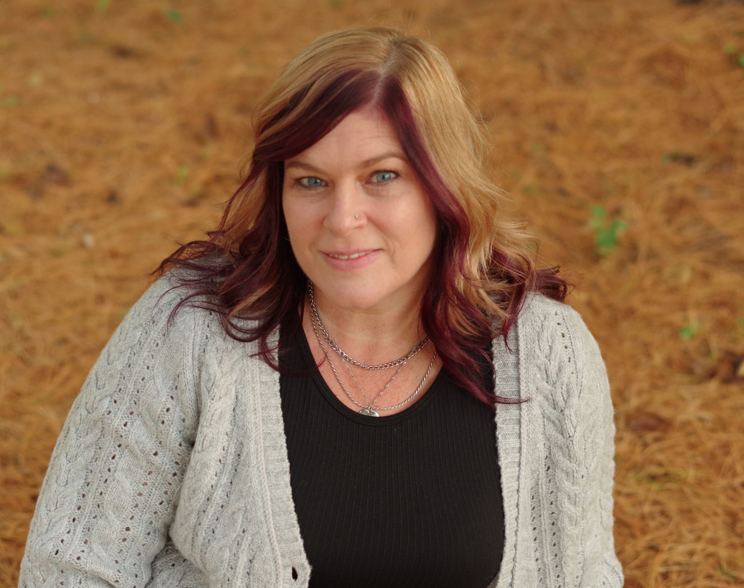 Portrait featuring person wearing black top and beige knit cardigan against orange autumn background.