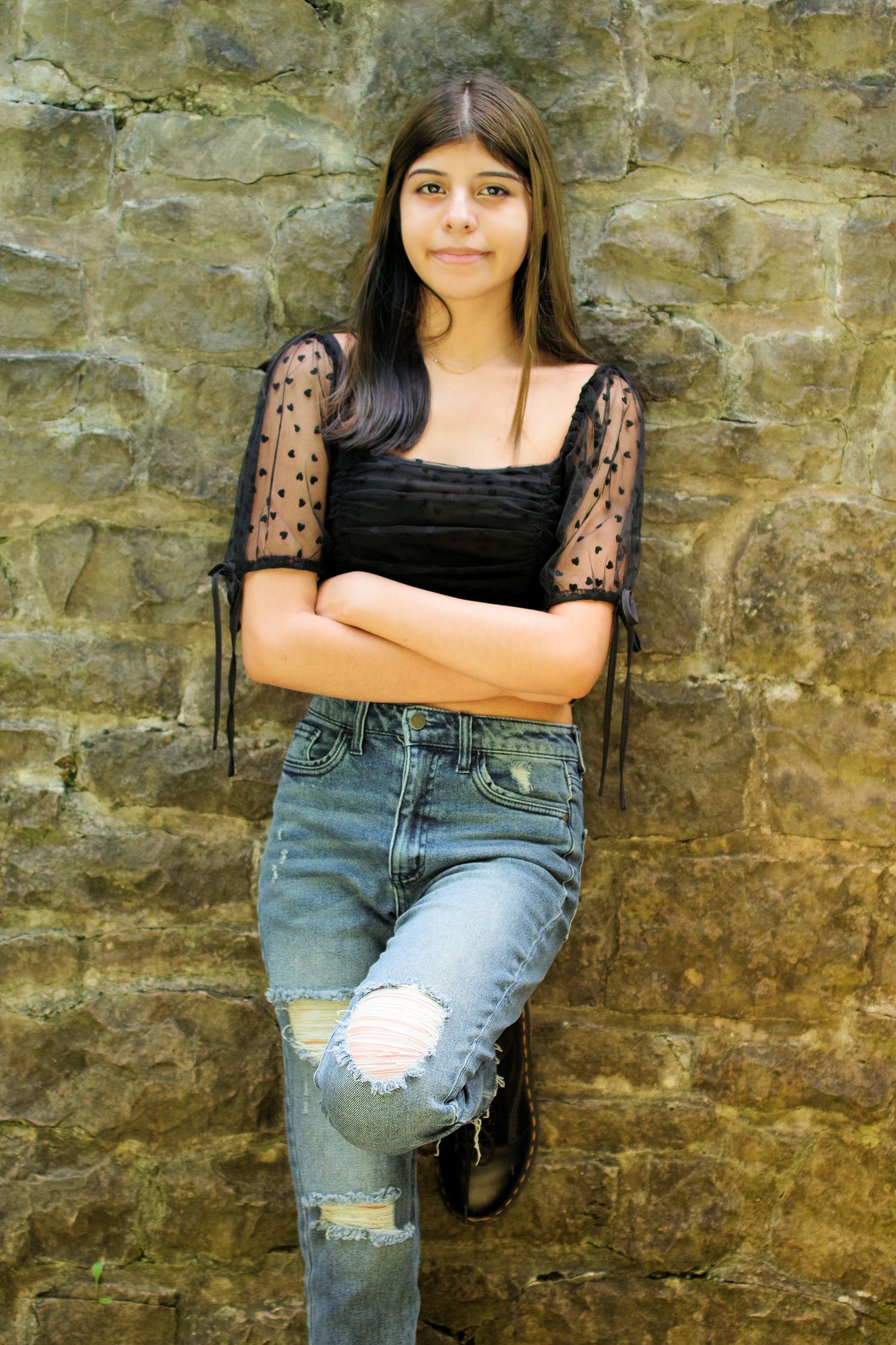 Casual portrait against stone wall wearing black lace top and distressed jeans.