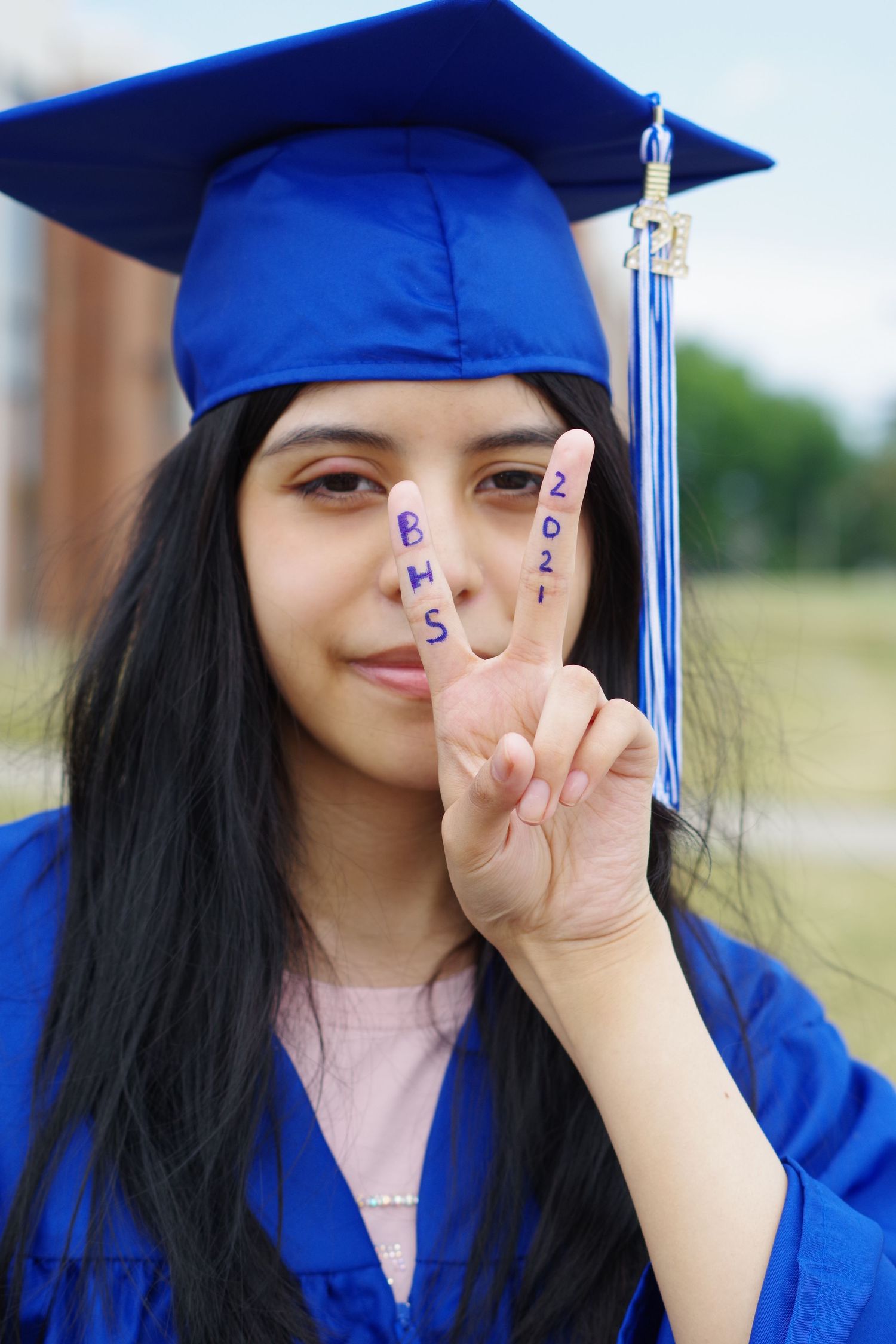 Graduate in blue cap and gown makes peace sign gesture during photo session.