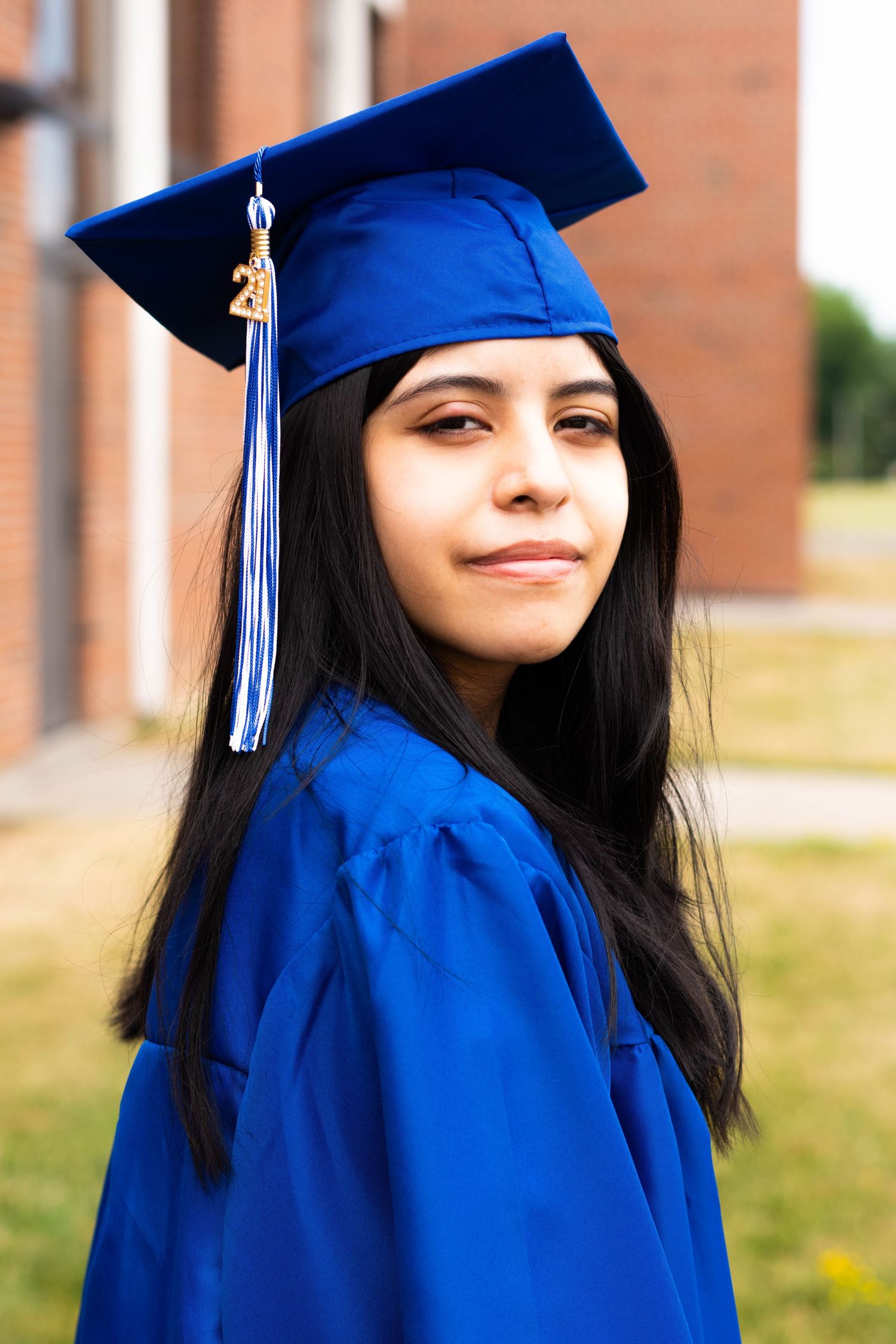 Graduate in royal blue regalia poses confidently against brick building.
